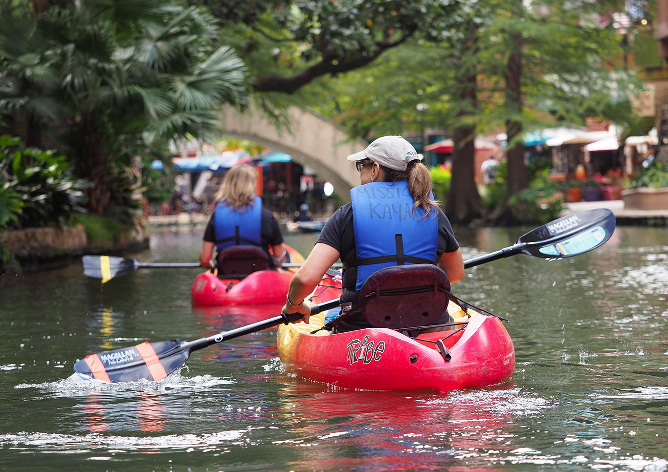 Kayakers paddle along the San Antonio River Walk during the day. 