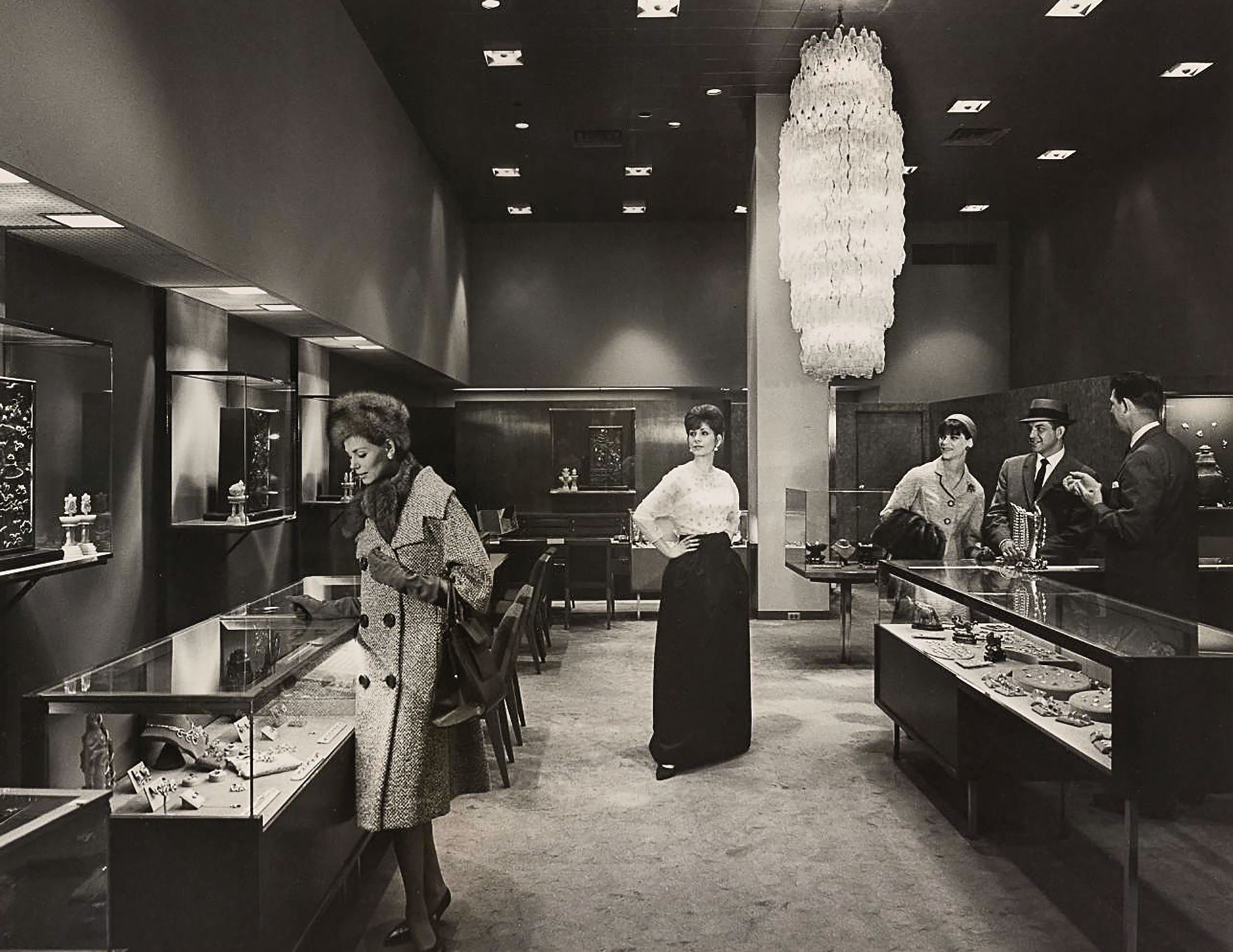 A woman looks at jewelry while others look on under a chandelier at Neiman Marcus
