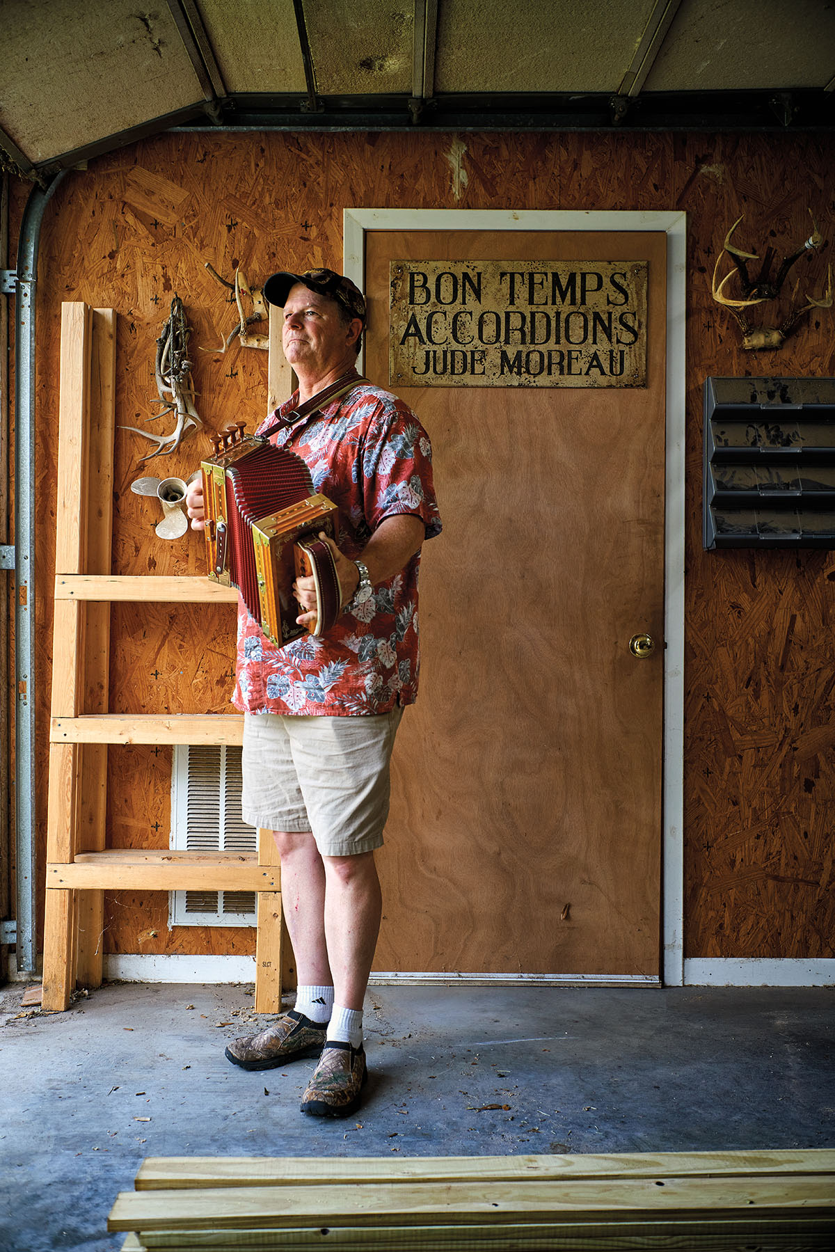 A man plays an accordion in front of a sign reading 'Bon Temps Accordions Jude Moreau'