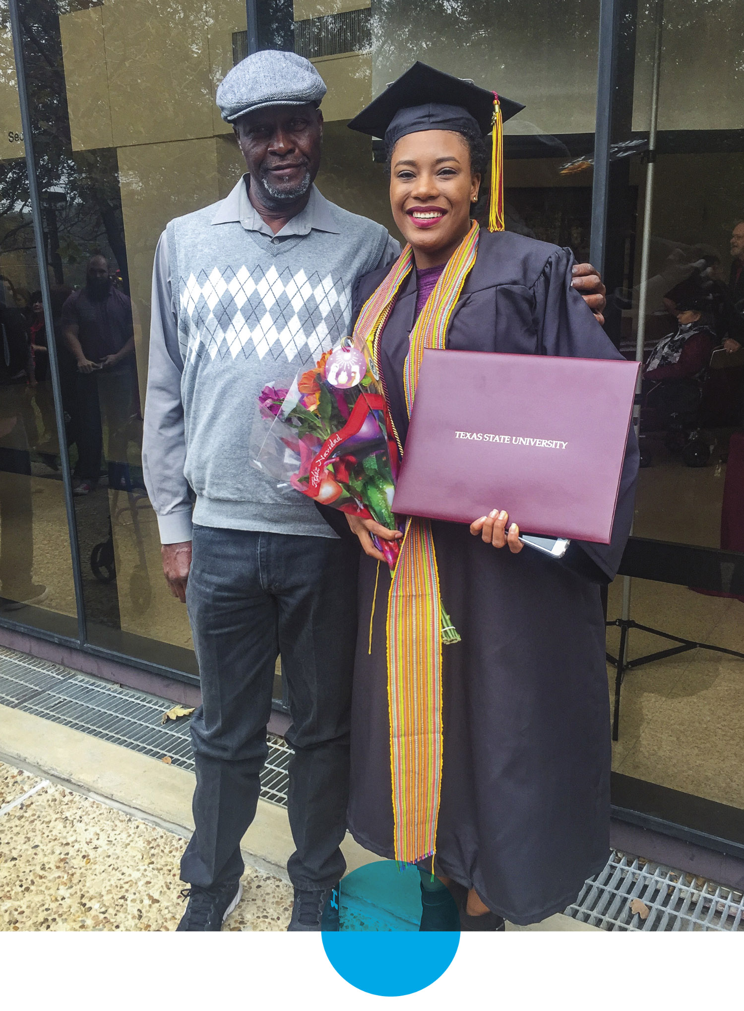 A woman in a graduation gown holds a diploma next to a man in a gray sweater