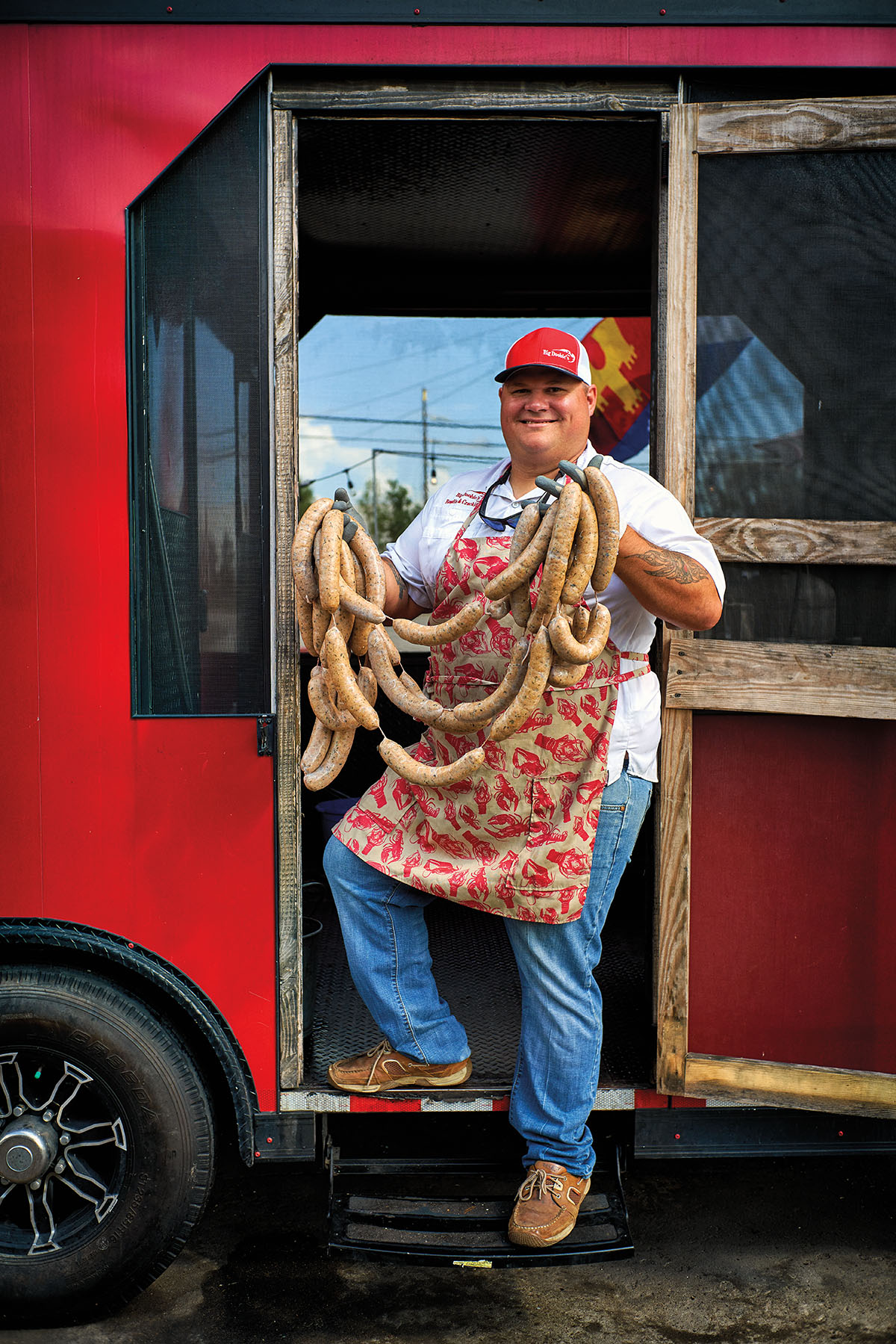 A man in a red hat holds a rope of sausage