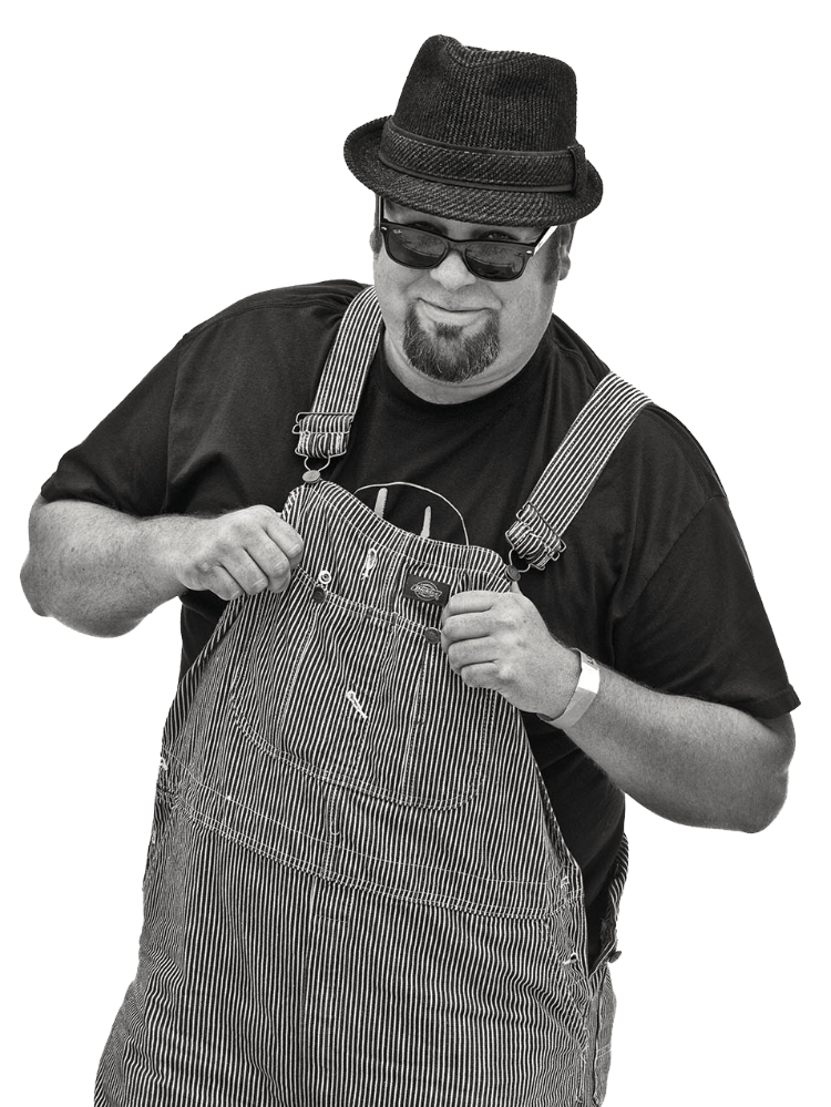 A man in a fedora and sunglasses poses in a pair of striped overalls