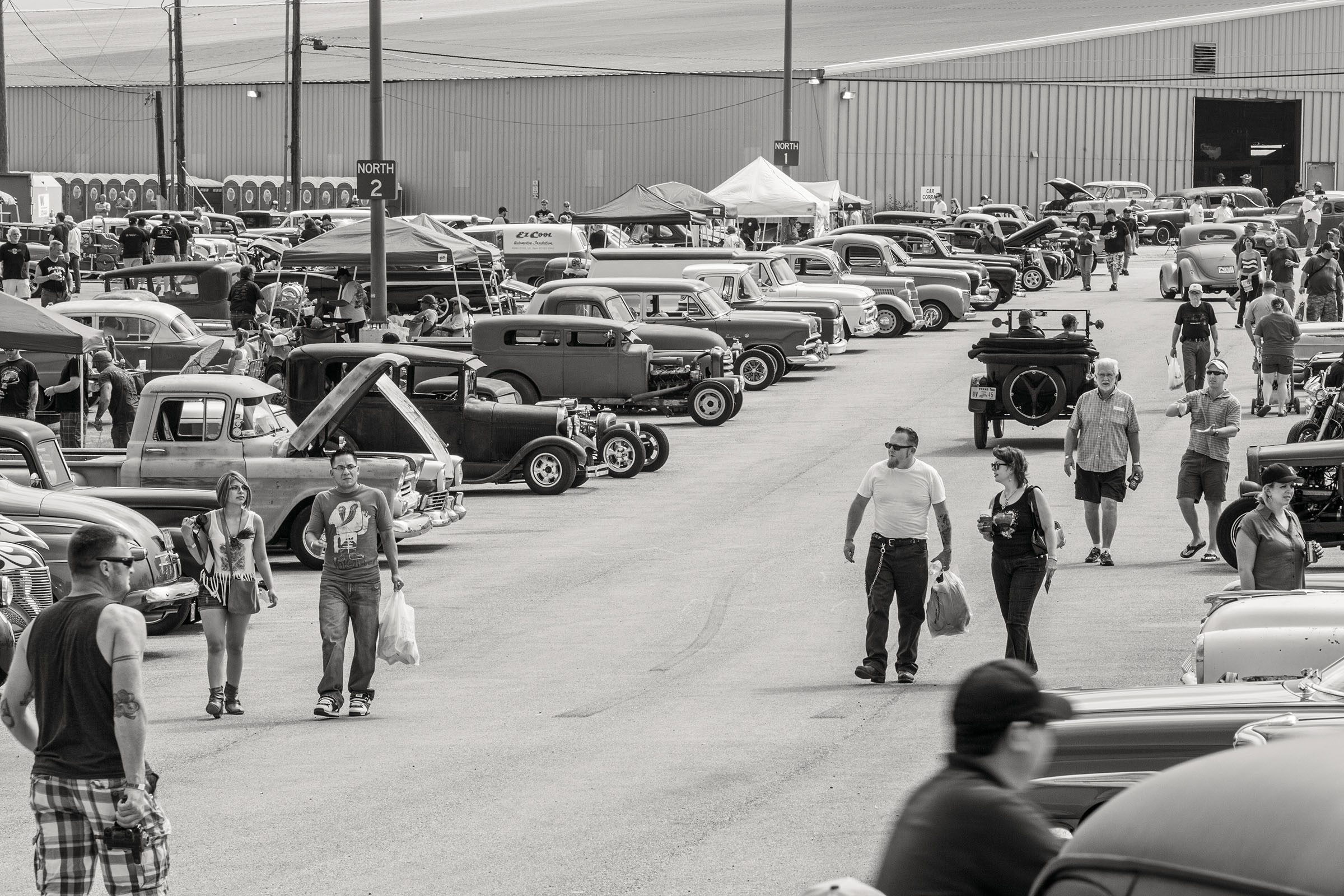 A few people walk down a dirt road in between rows and rows of historic cars