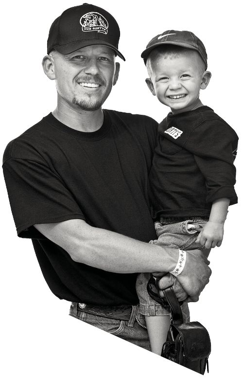 A man in a ball cap holds his son in his arms, also wearing a baseball cap