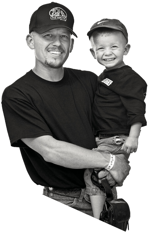 A man in a ball cap holds his son in his arms, also wearing a baseball cap