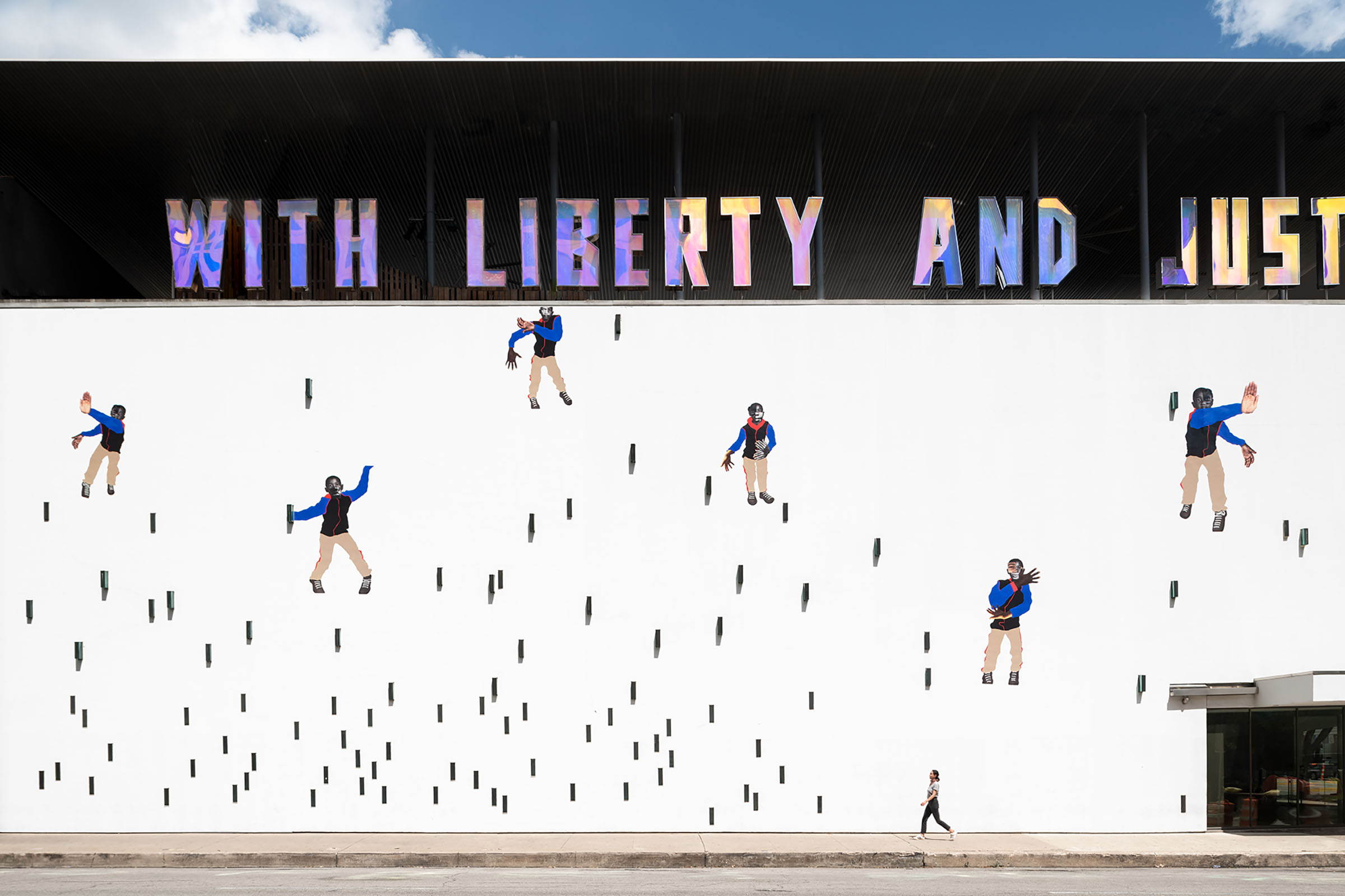 The wall of The Contemporary Austin reading "With Liberty and Justice" with a mural below and a person walking by