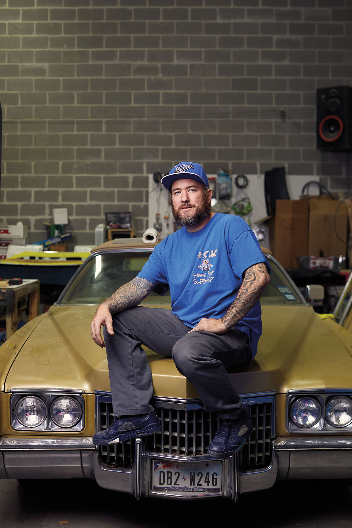 A man in a blue baseball cap and shirt sits on the hood of a mustard-yellow car