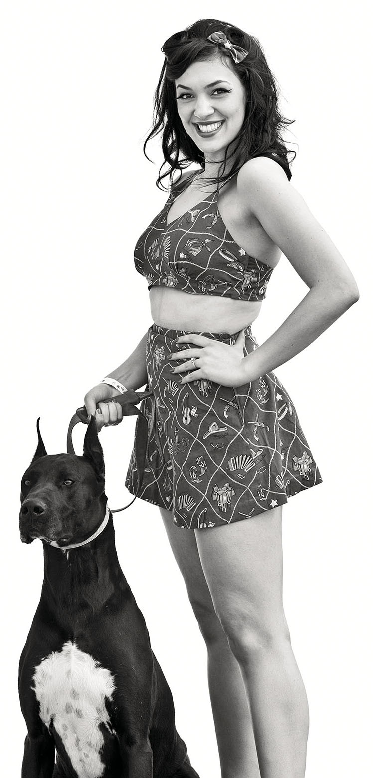 A woman stands holding a tall black dog on a leash