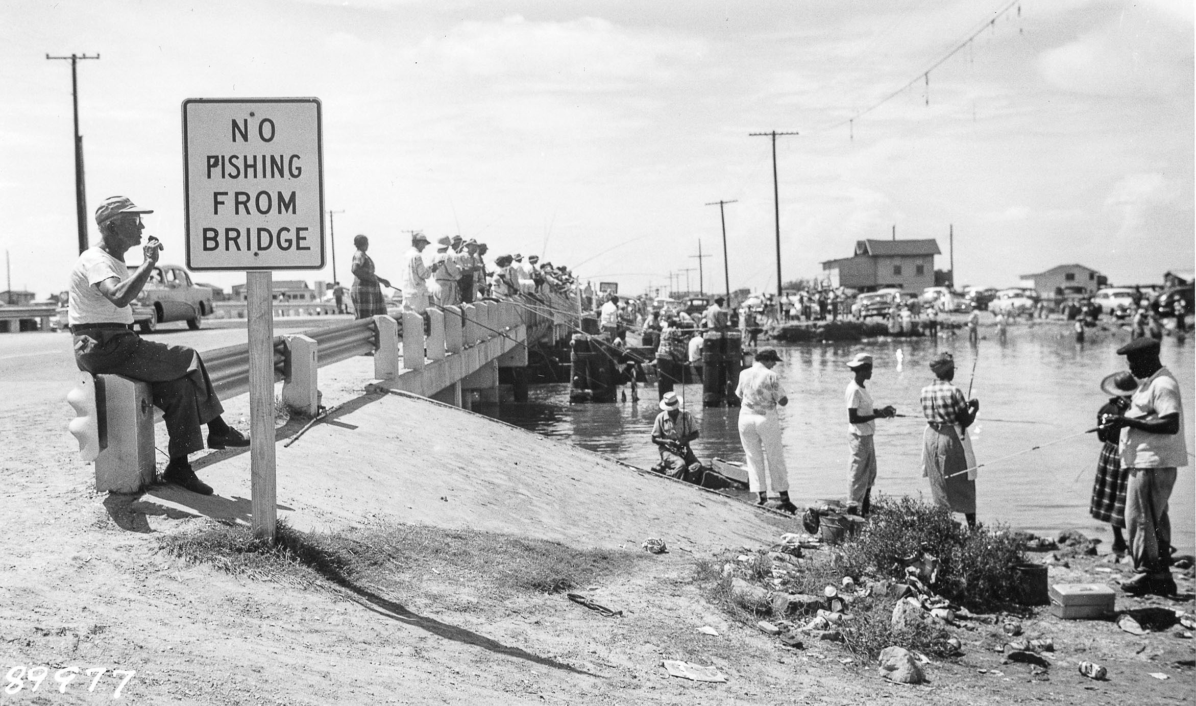 A large group of people stand around and fish from a road bridge