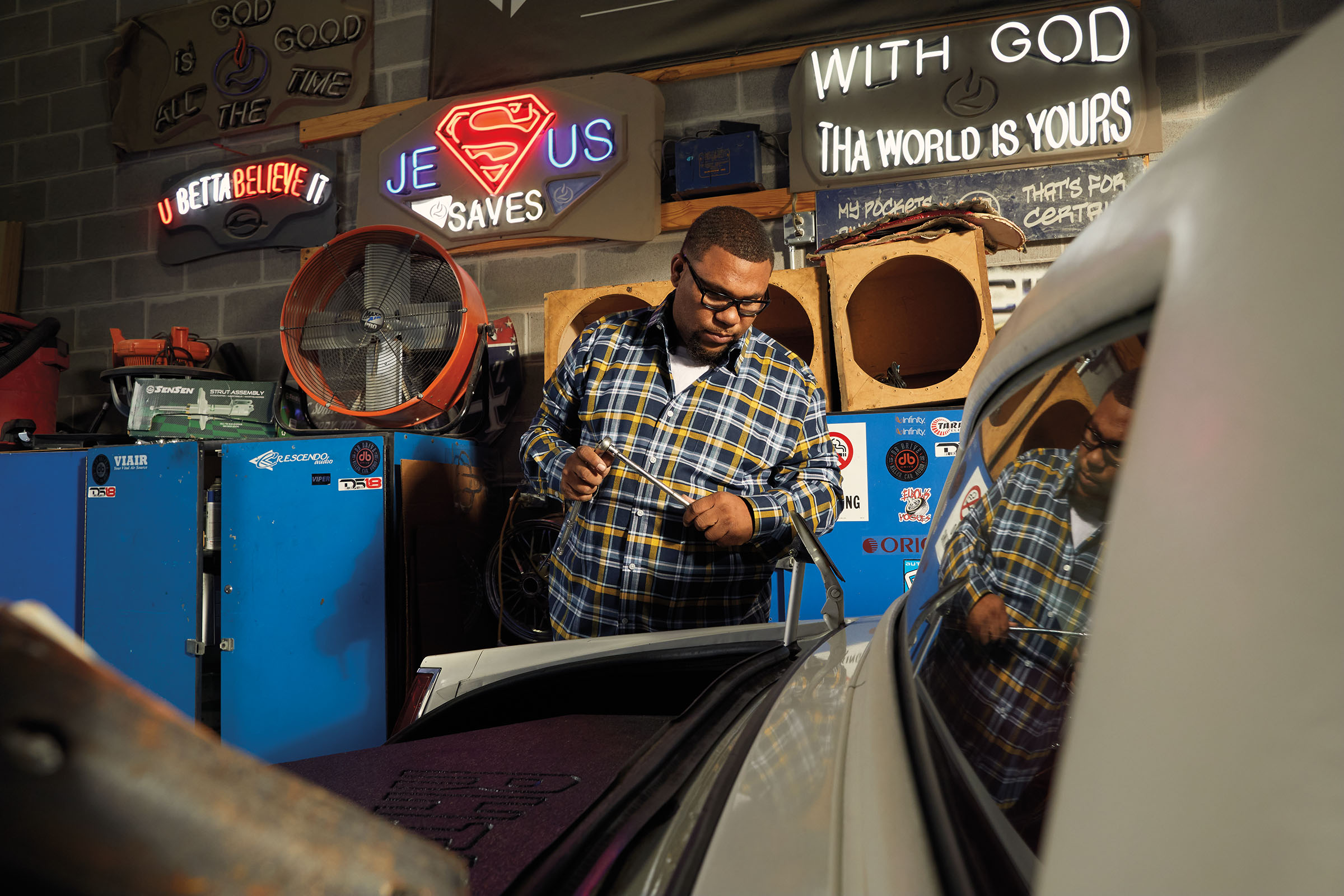 A man holds a tool while looking over the open hood of a white car in a garage