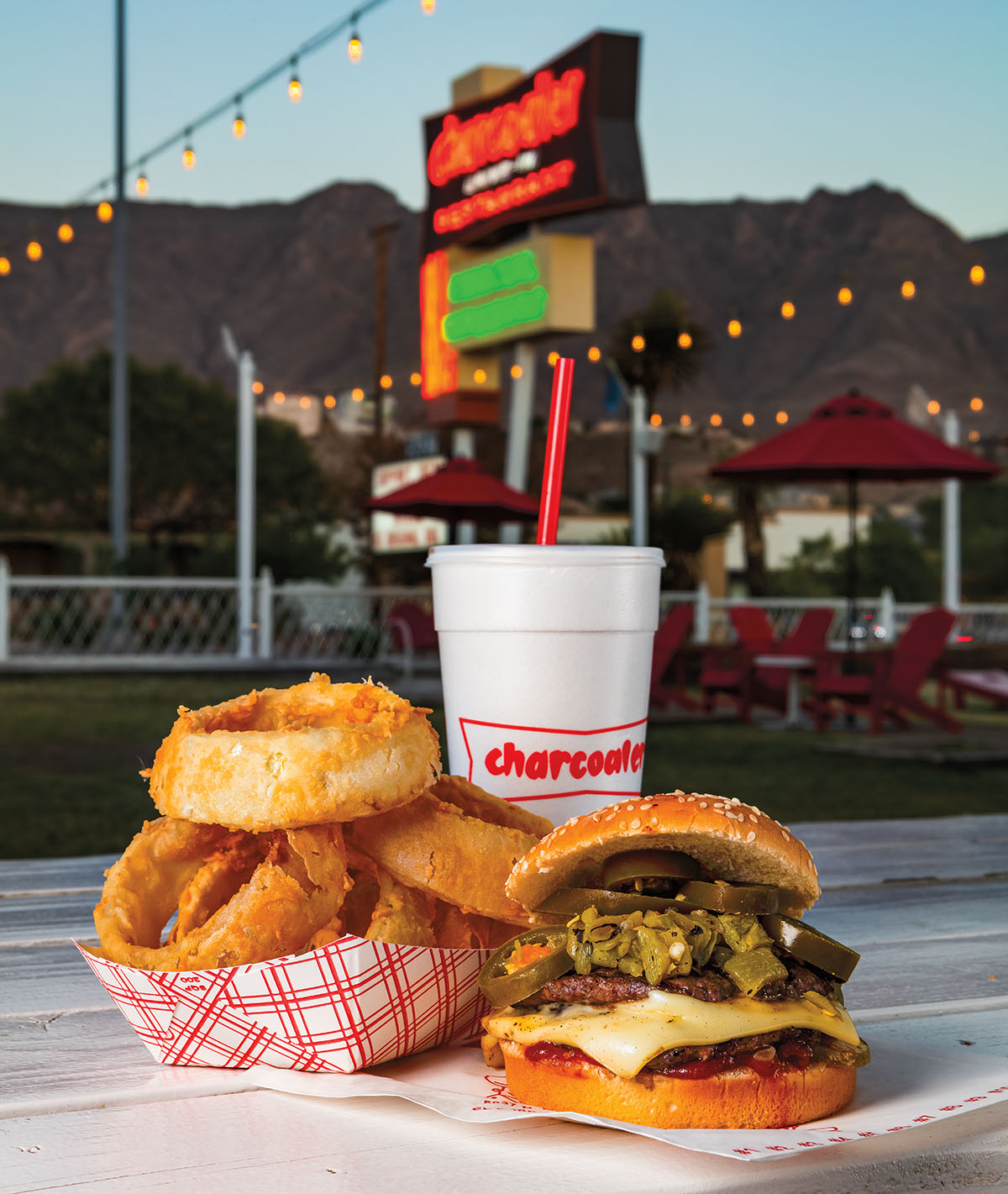 A serving of onion rings, a cheeseburger and drink in a styrofoam cup underneath the Charcoaler's sign