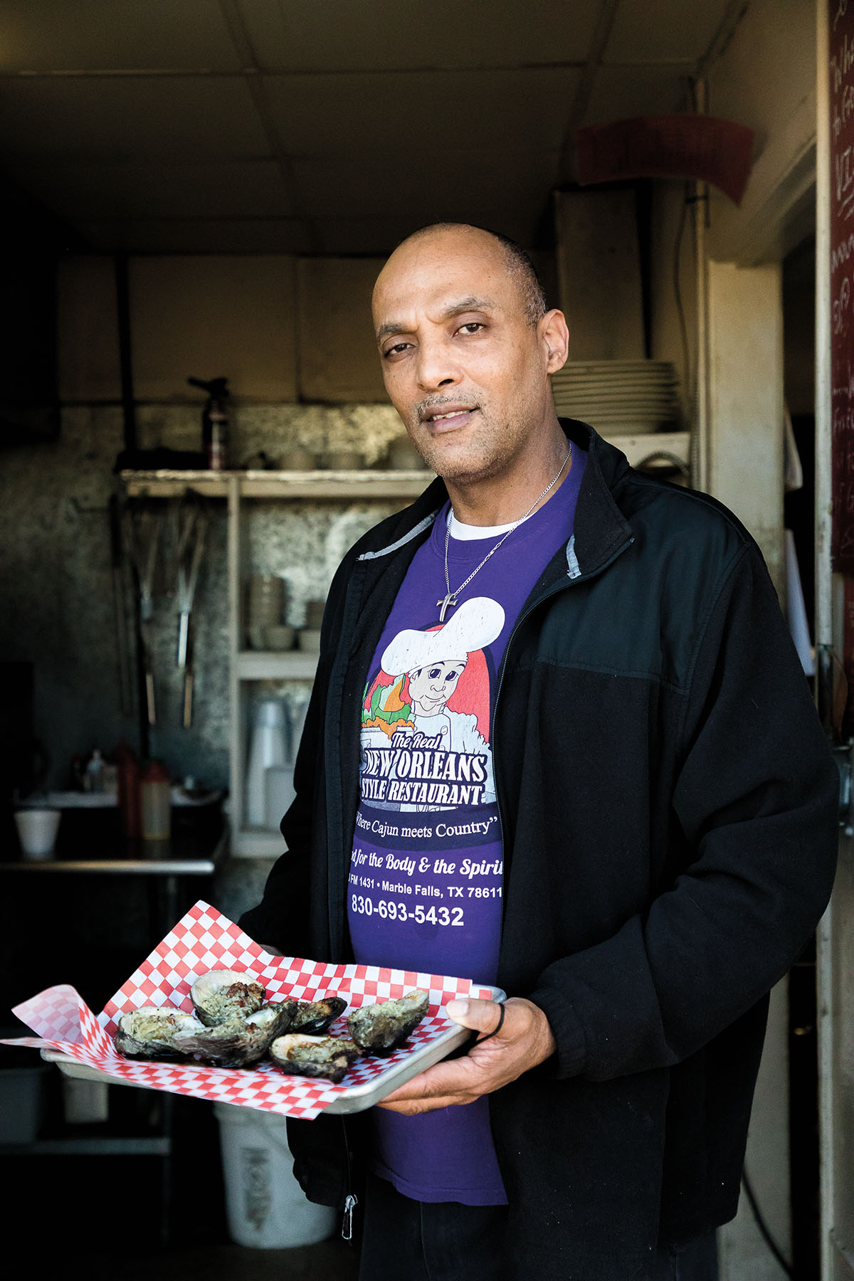 A man in a purple shirt and black jacket holds a platter of oysters