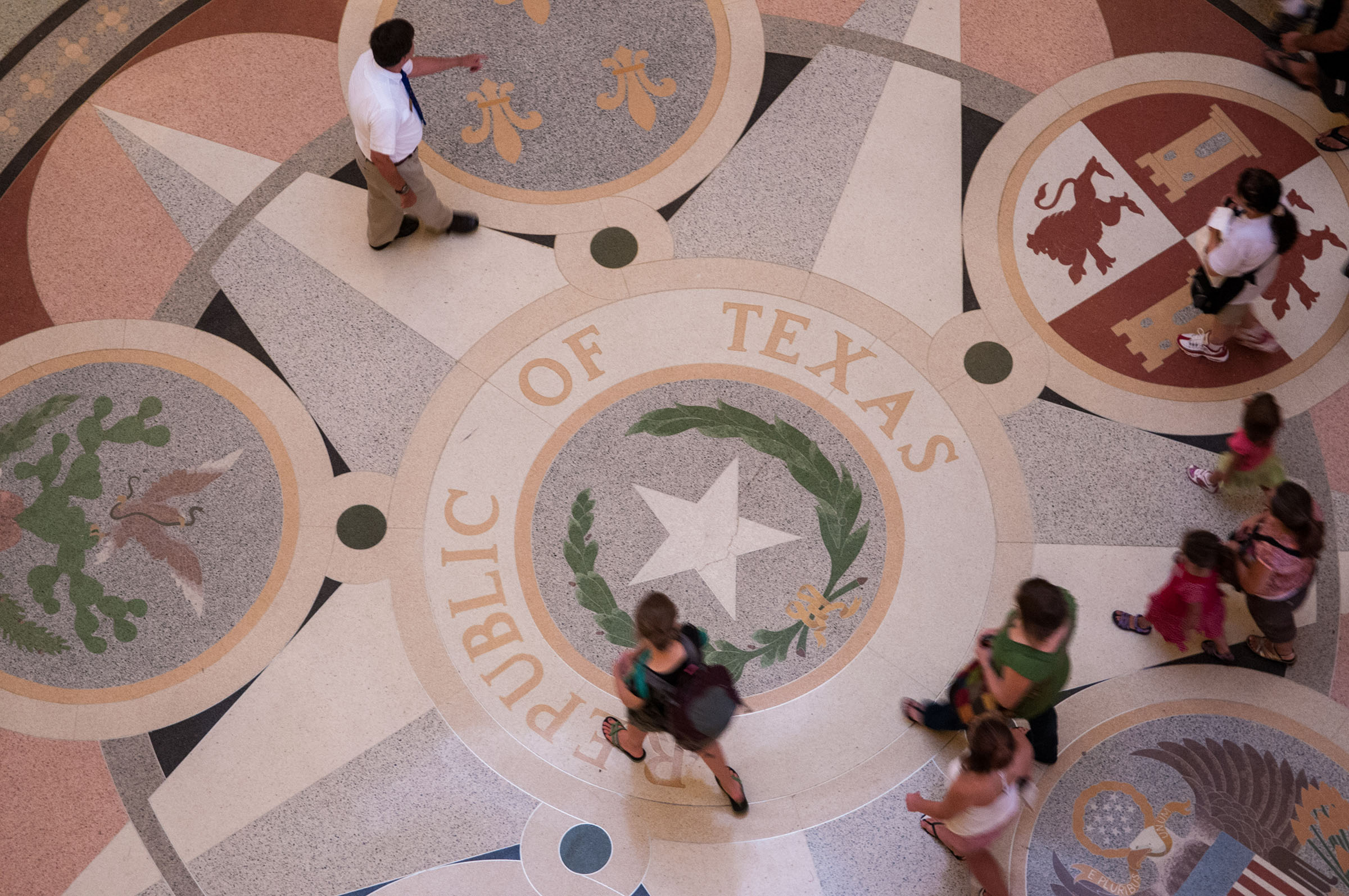 A small group of people walk across a decorative floor reading "Republic of Texas"
