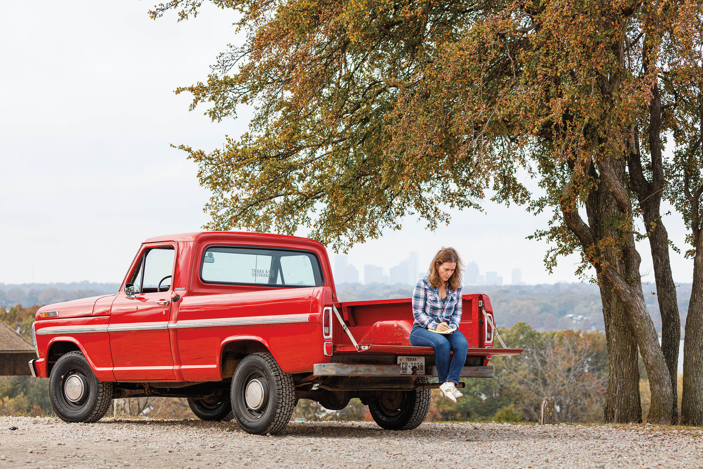 The author sitting on the tailgate of a red truck on a dirt road with a city skyline in the background