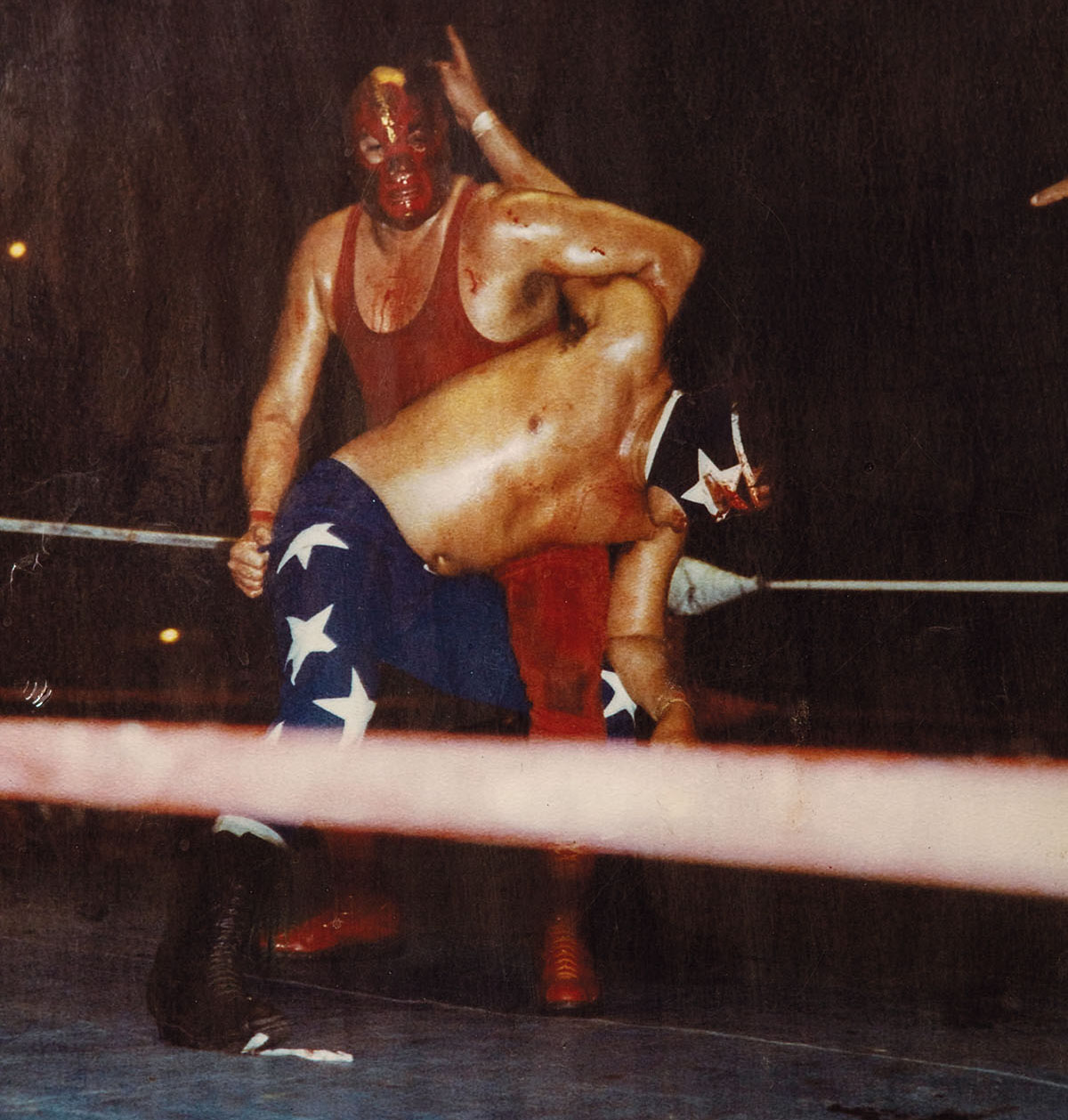 A man in red and a man in striped pants fight in a boxing ring