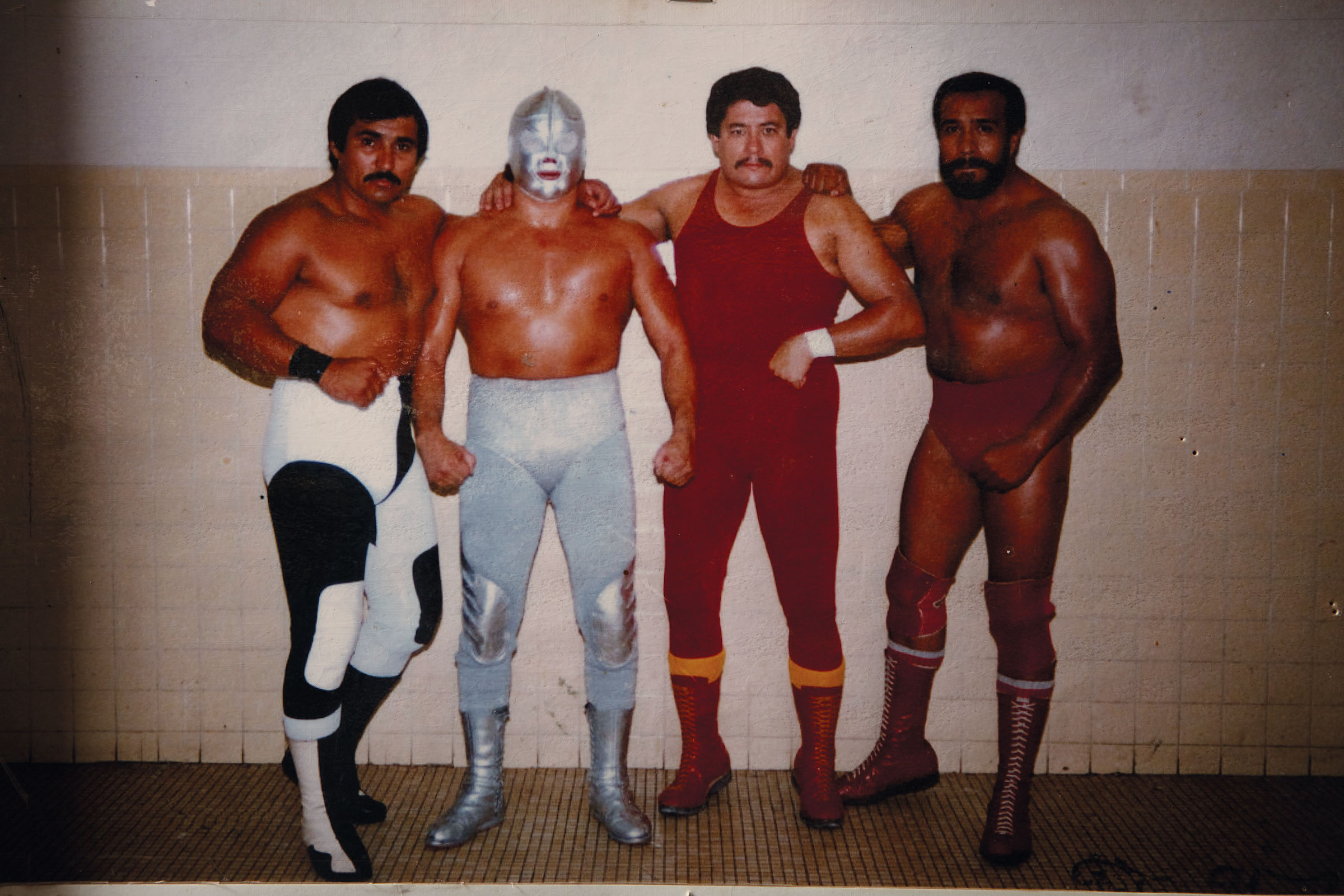 A group of men dressed in lucha libre uniforms pose in front of a wall