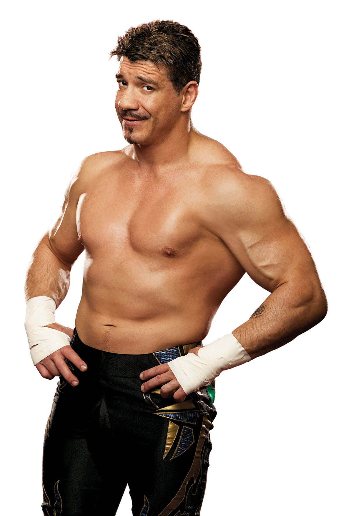 A shirtless man with white wraps on his wrist and black pants poses for the camera on a white background
