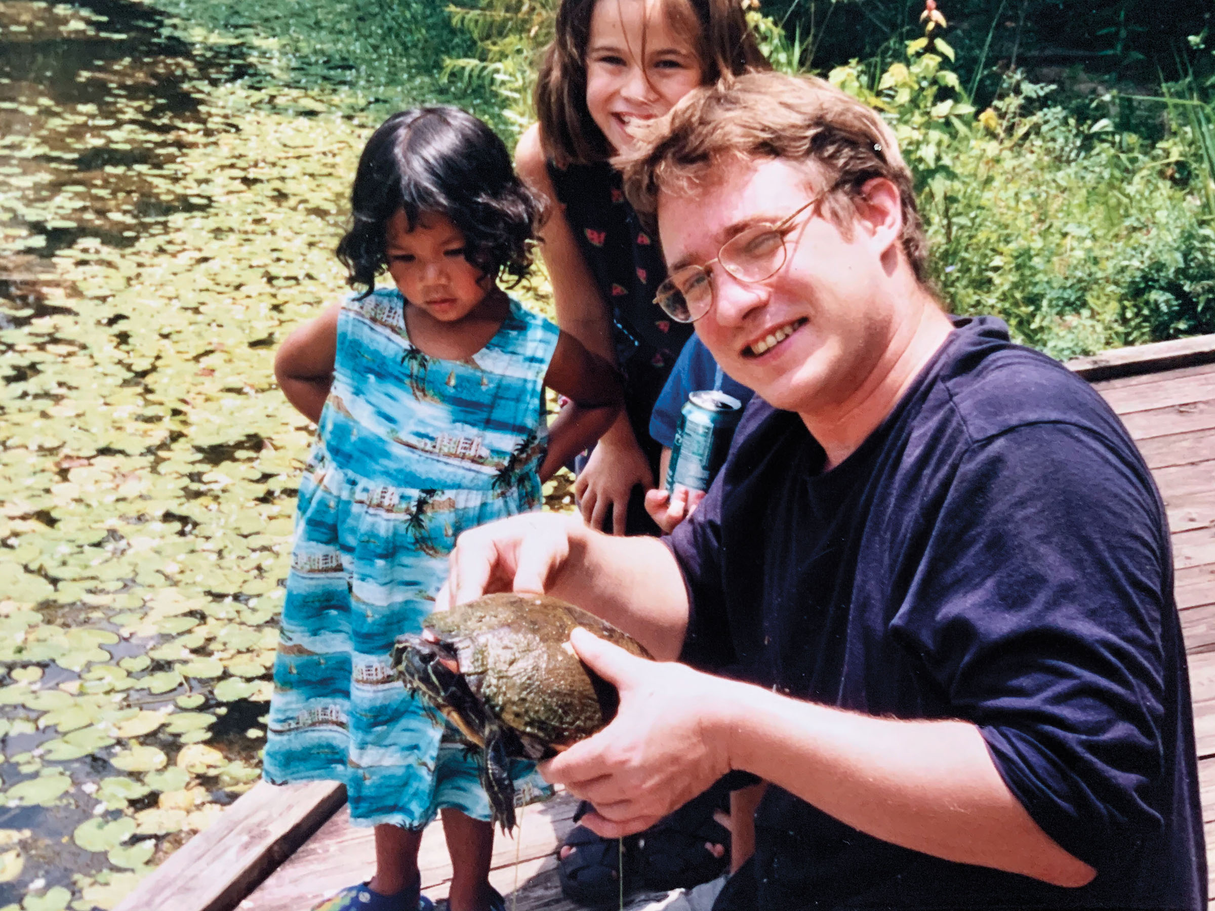 A man in a blue shirt holds a turtle in front of two young children