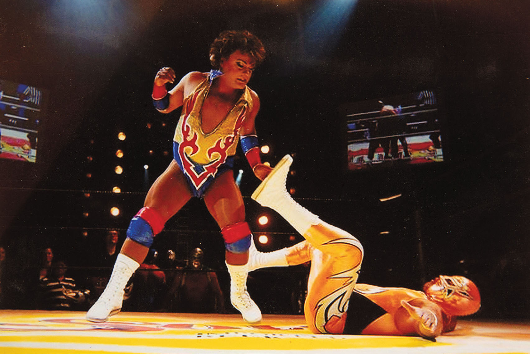 Two people in brightly-colored lucha libre costumes in a ring