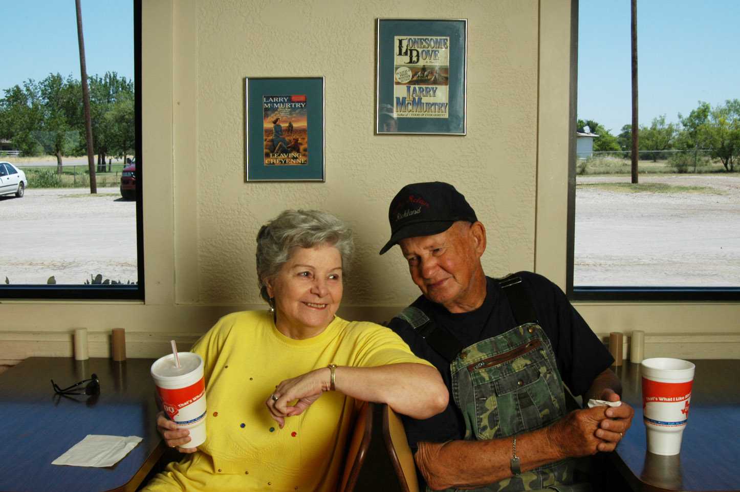 Two people sit at a Dairy Queen underneath framed covers of Lonesome Dove.