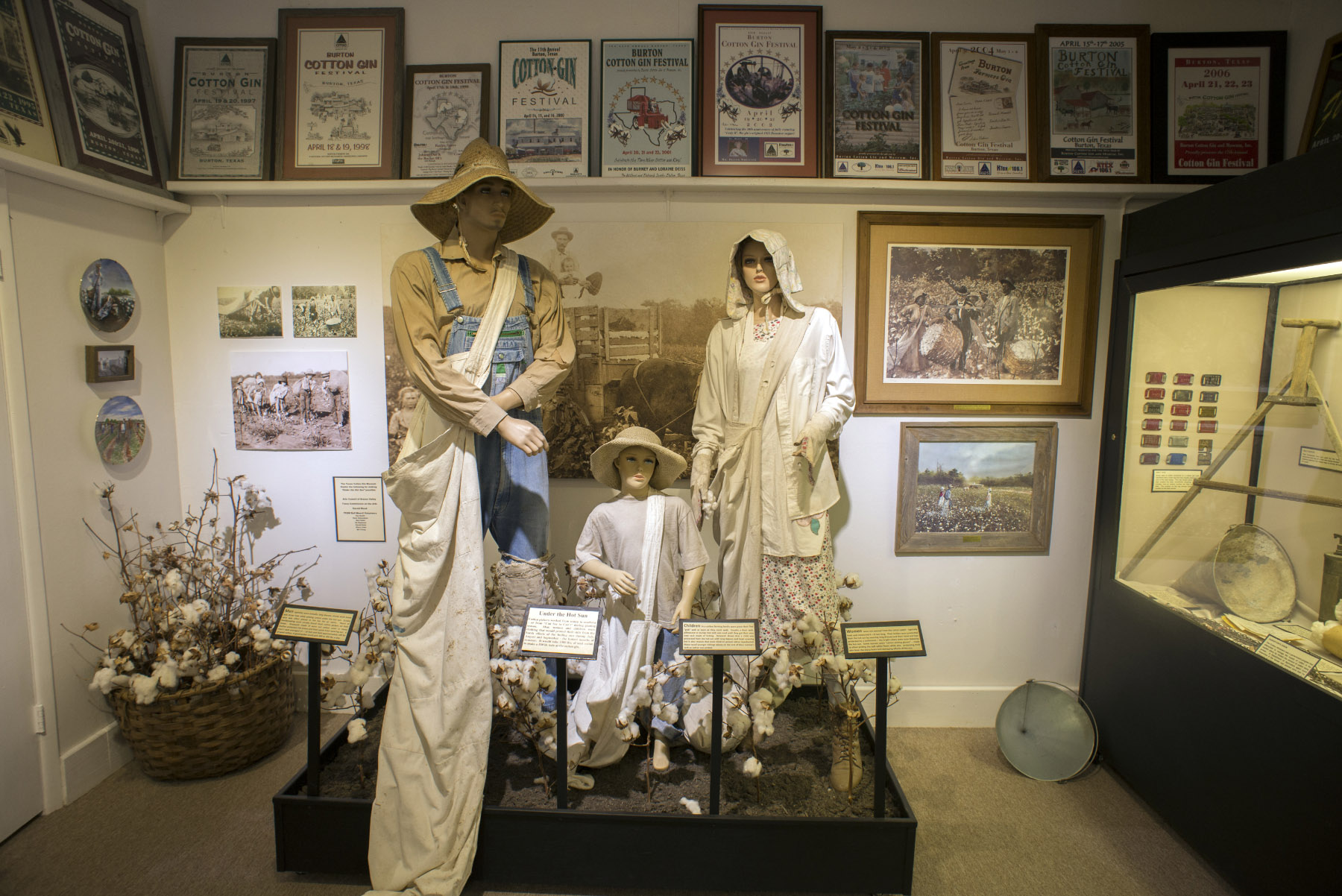 Mannequins dressed in old-timey farm attire stand on a platform in front of a wall lined with old photos and posters at the Texas Cotton Gin Museum in Burton. Photo by Kevin B. Stillman.