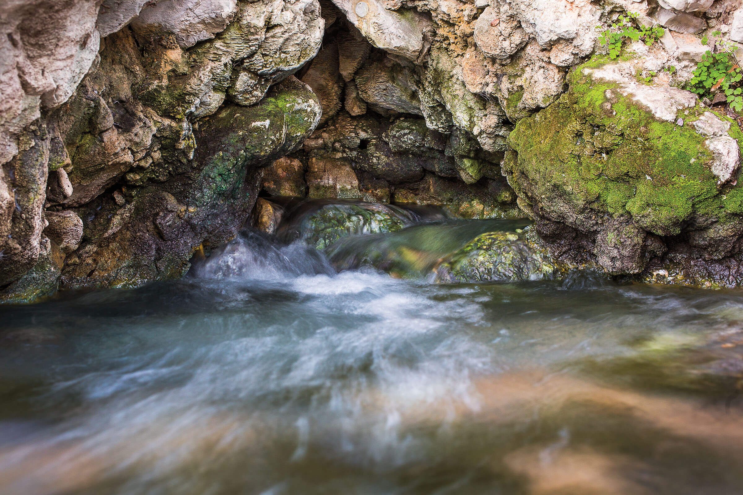 Cool blue water flows under gray rocks and bright green moss