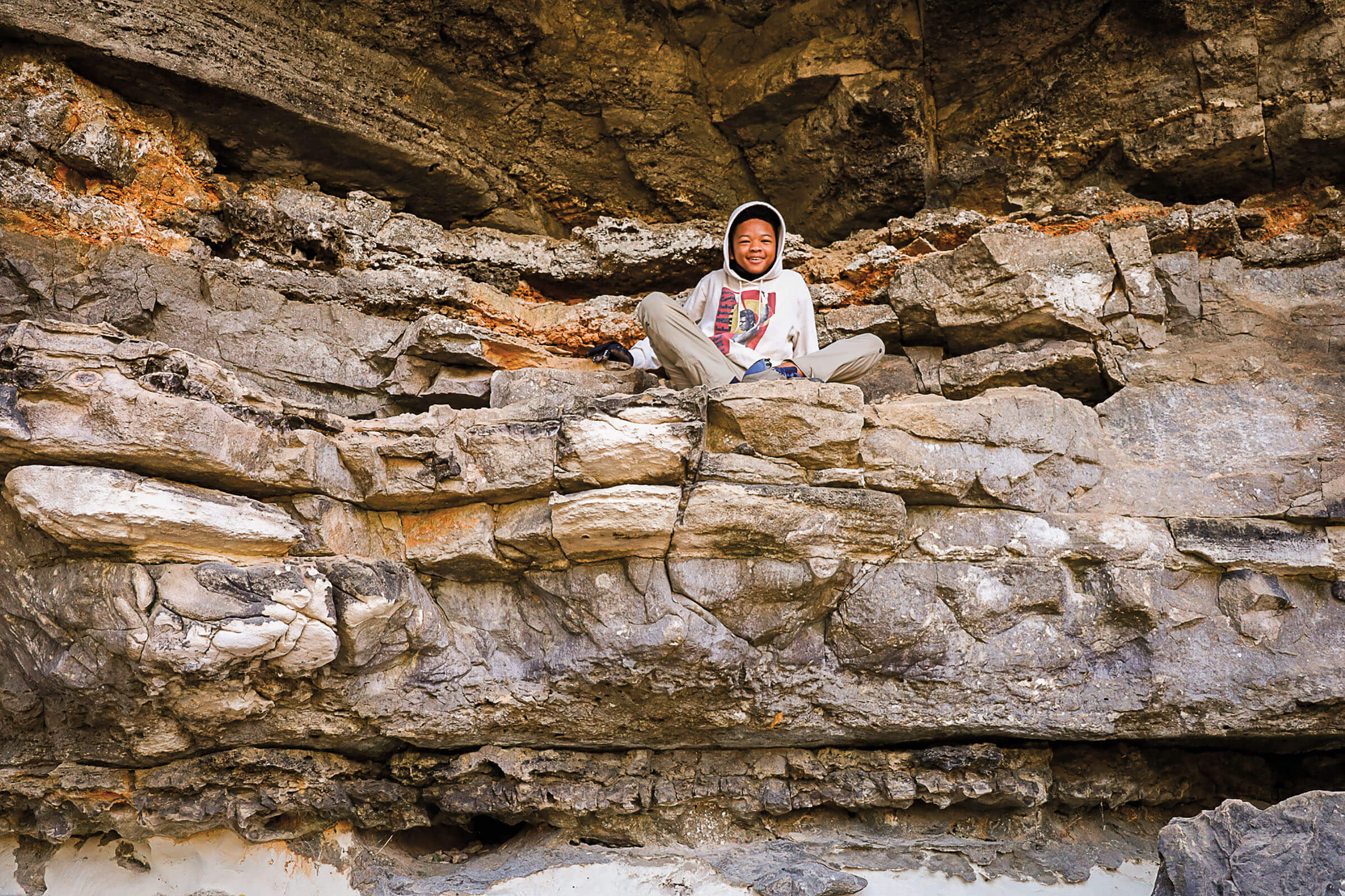 A young man in a sweatshirt sits up high on a stack of rocks