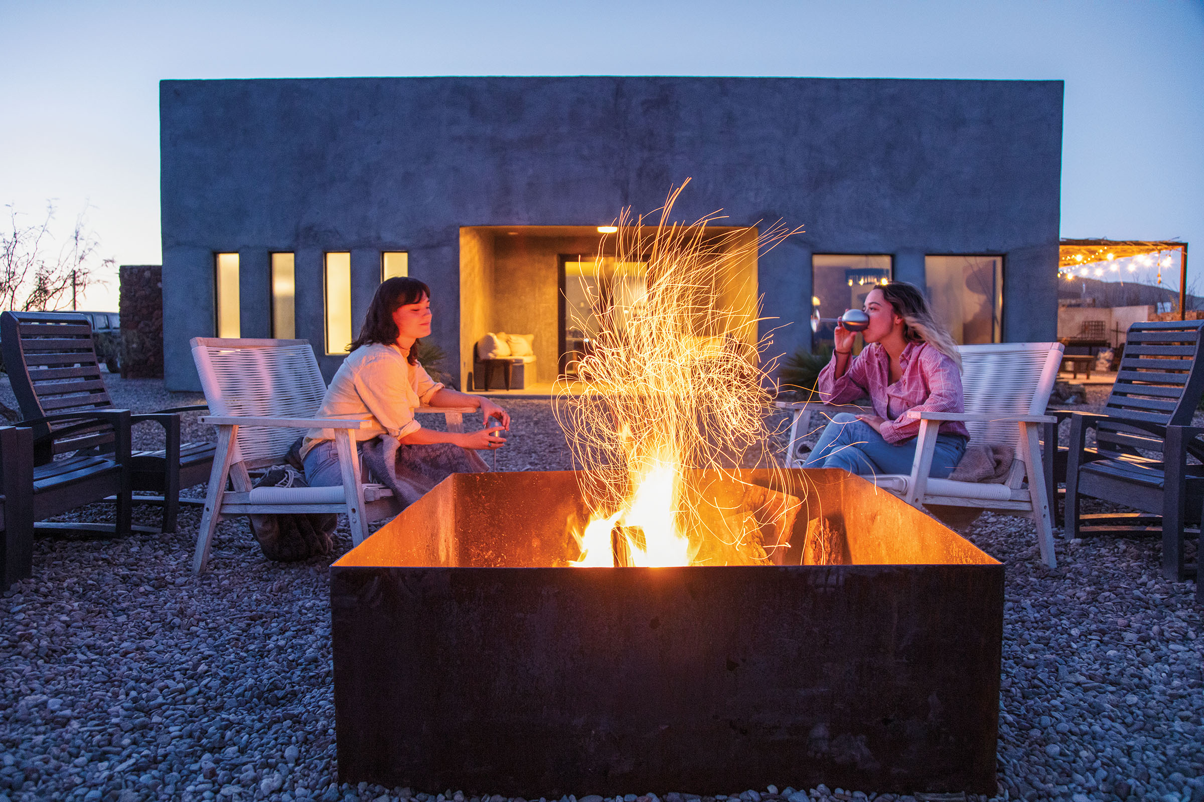 Two women hold wine glasses in the glow of a yellow-orange fire