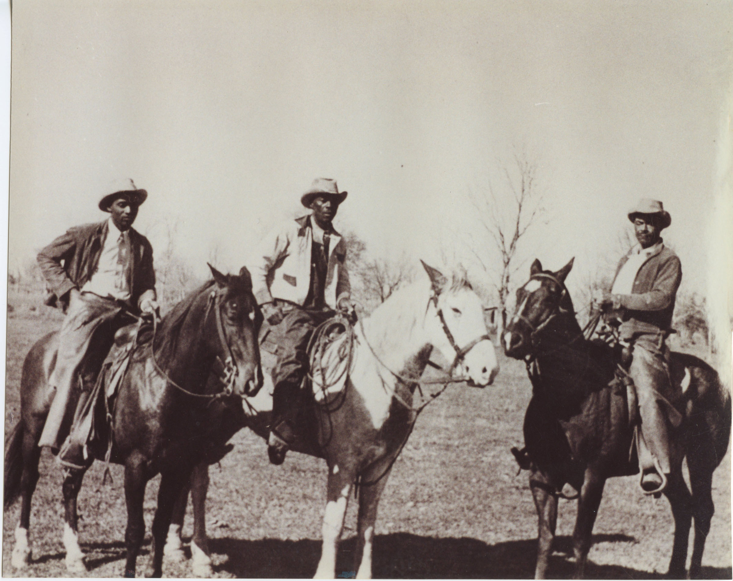 Three men on horseback in small cowboy hats in a barren landscape with one tree