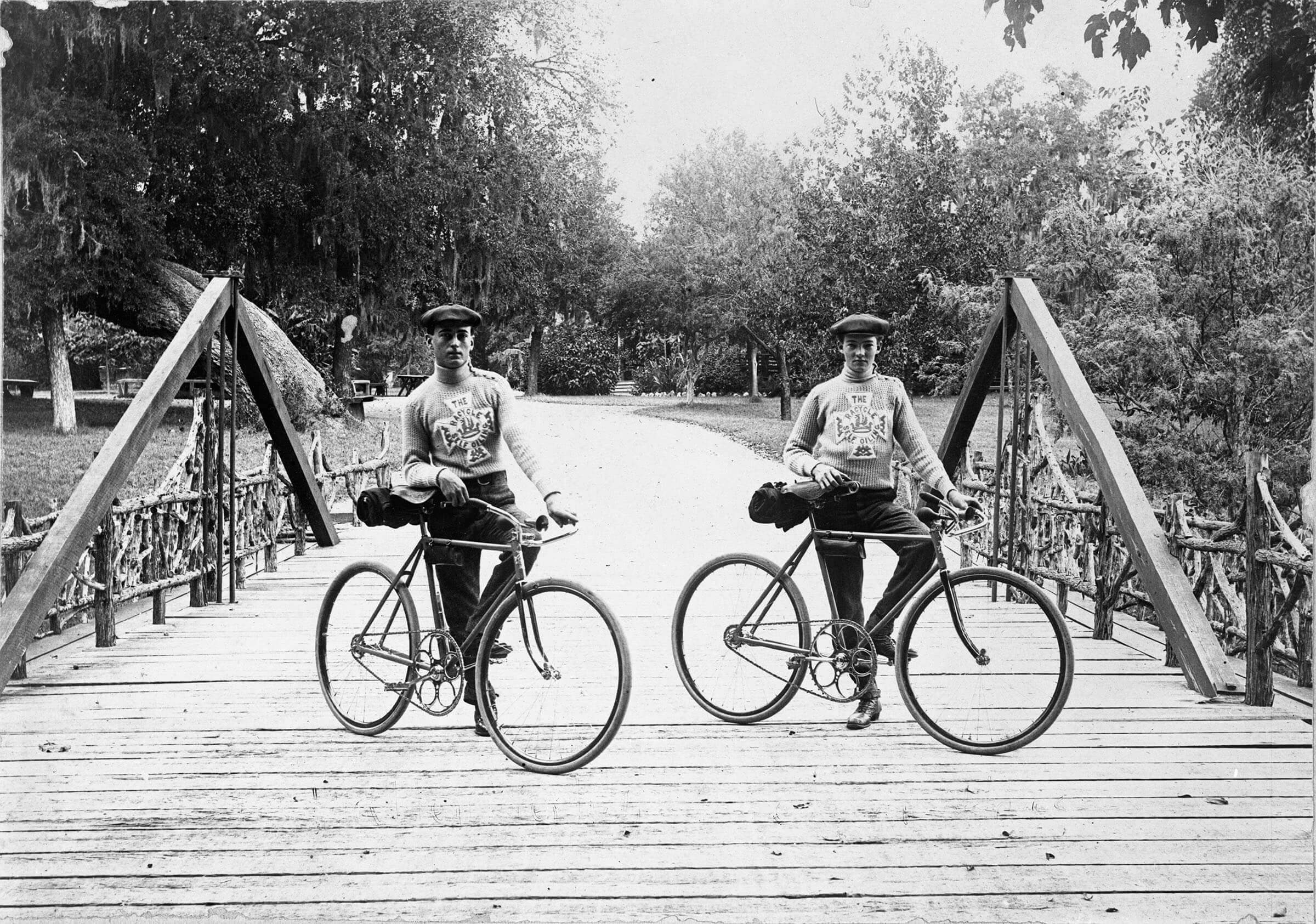 Two men stand on bicycles on a wooden bridge