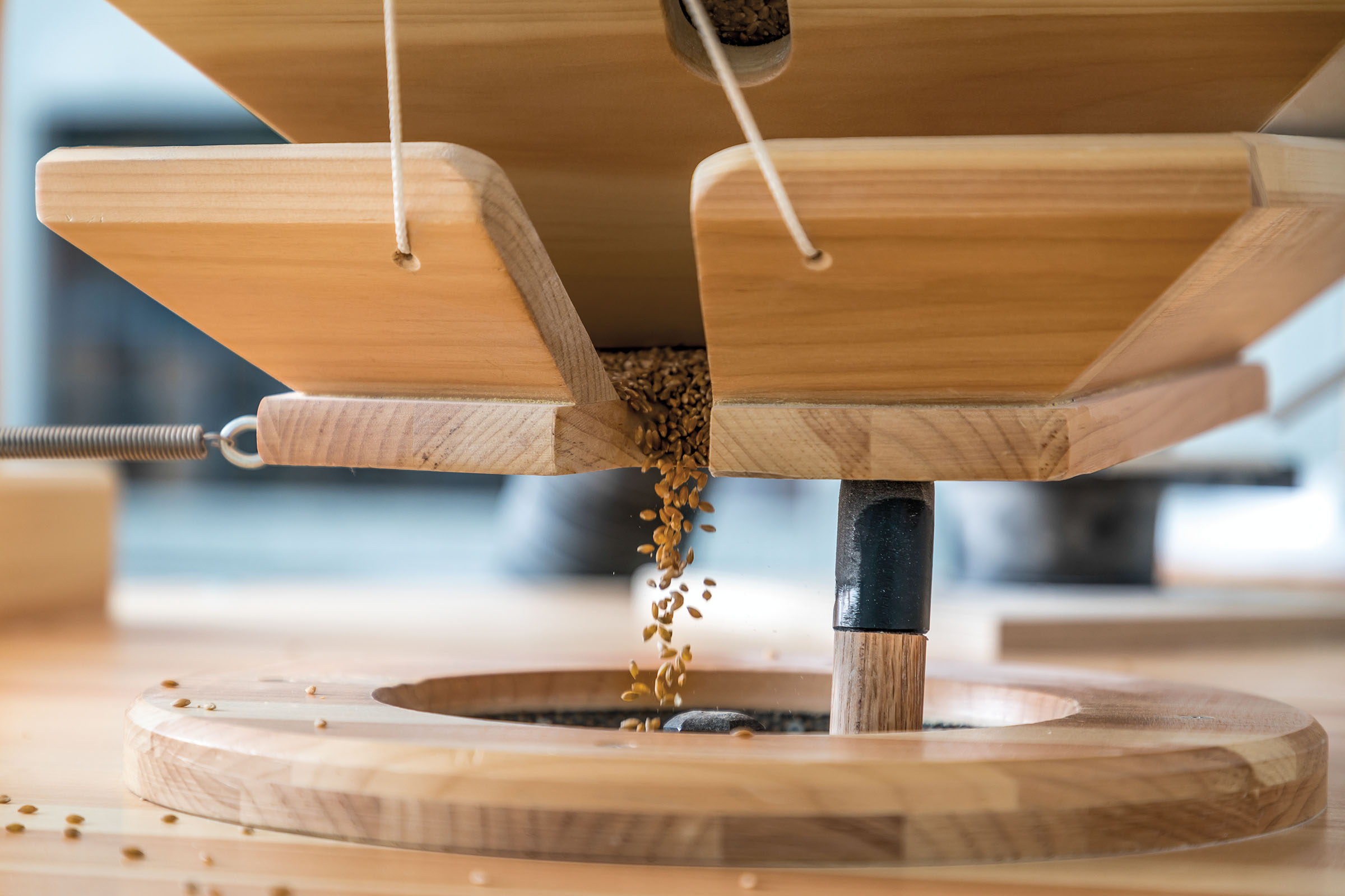 Small kernels of grain pass through a wooden hopper into a mill