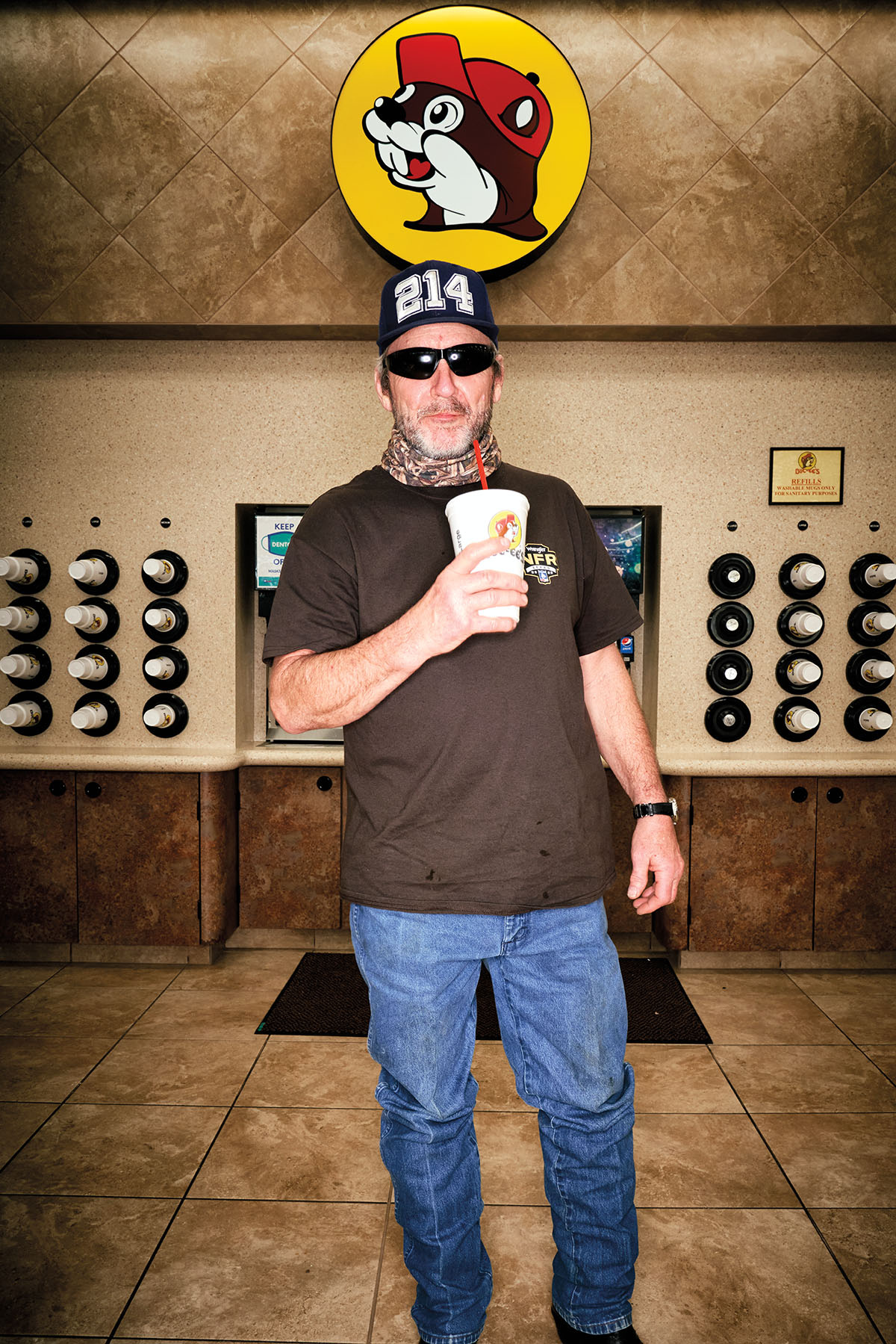 A man in a 214 hat stands underneath the Buc-ees insignia holding a fountain drink