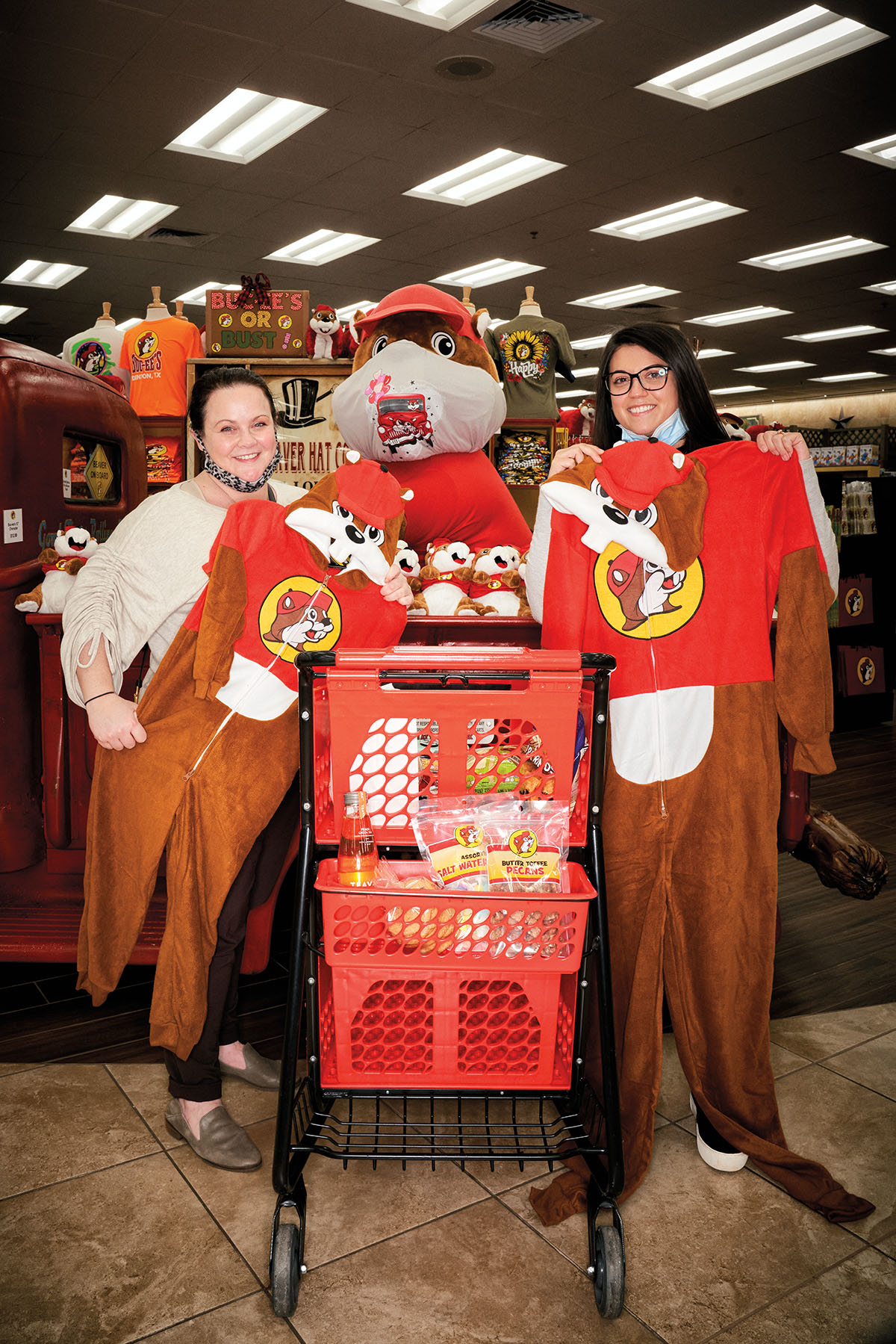 Two women pose with Buc-ees onesies in front of a stuffed beaver
