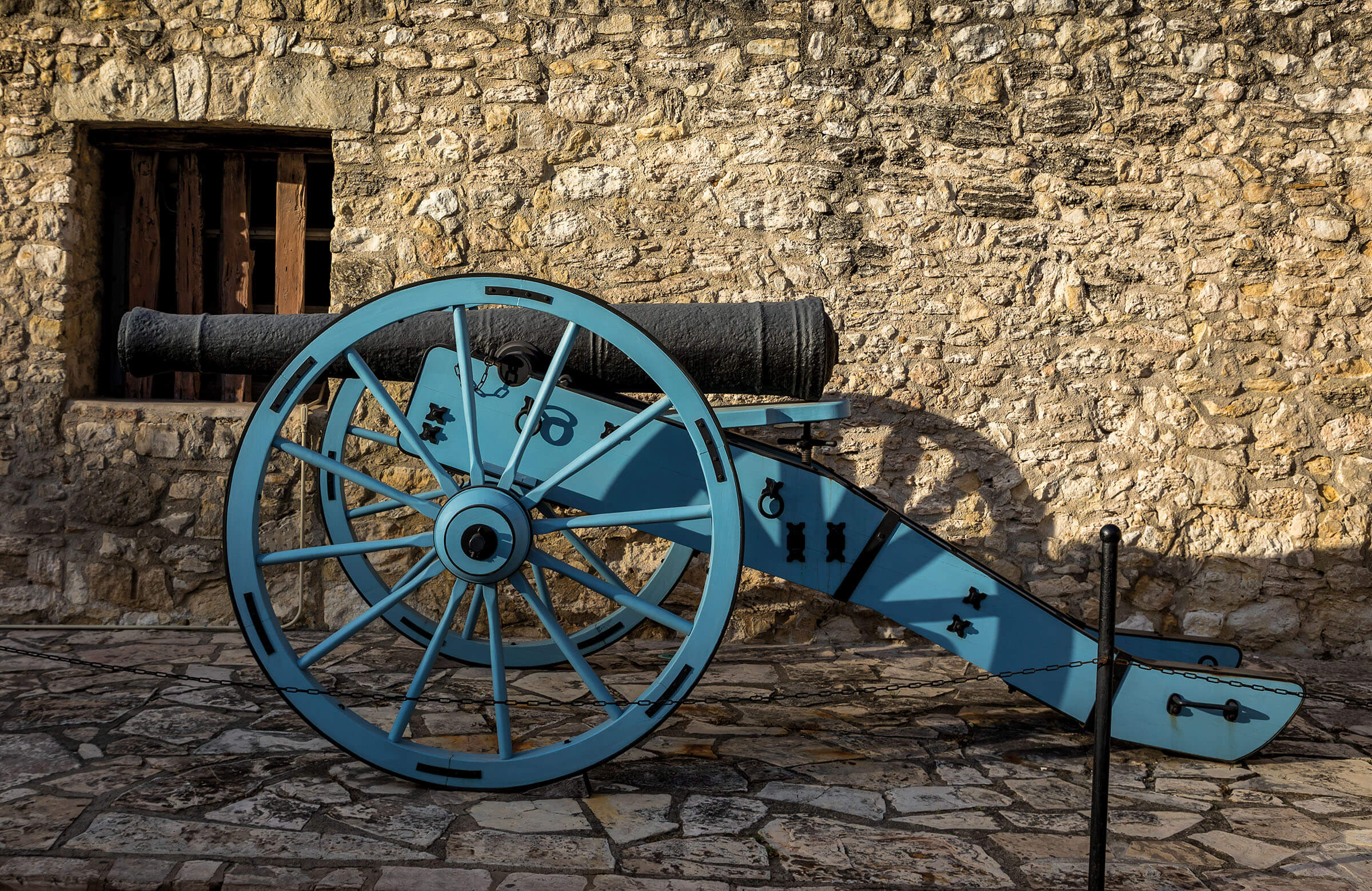 A turquoise cannon in front of a stone wall