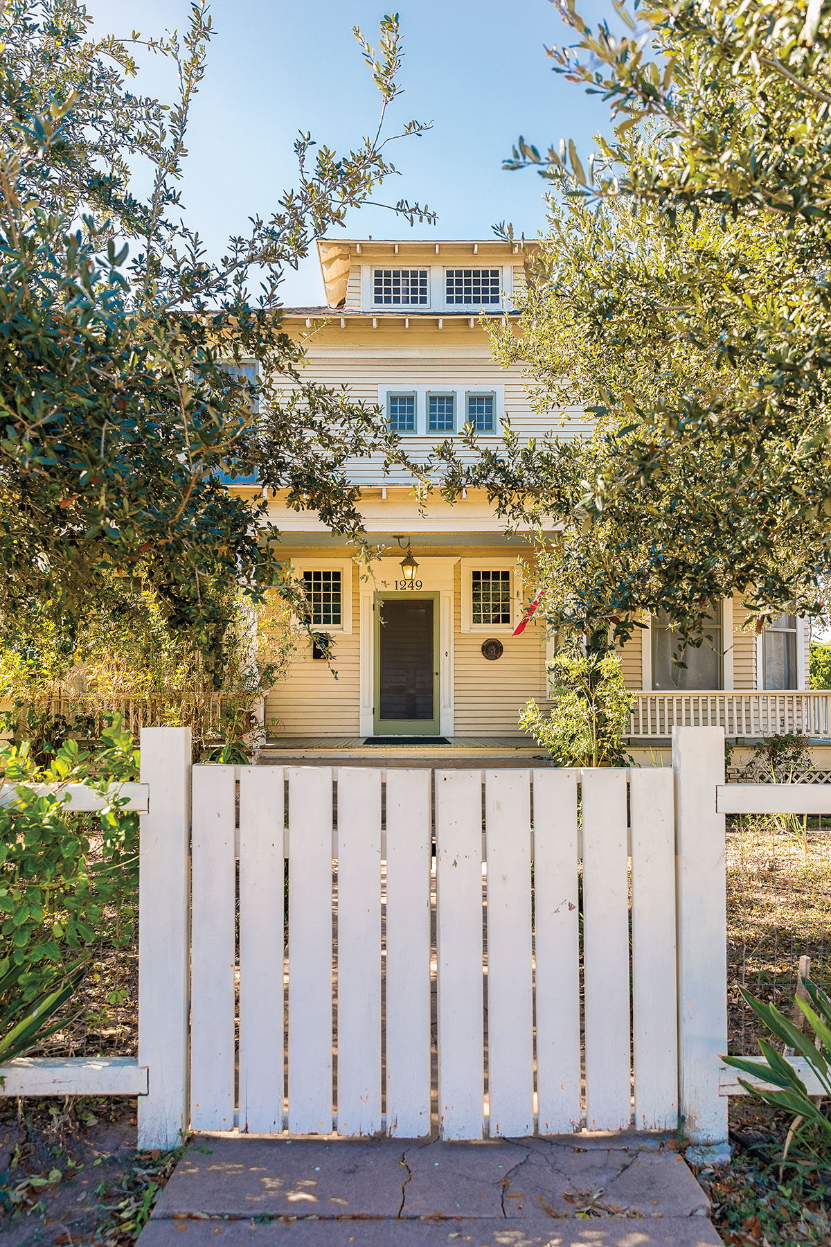 The exerior of a historic yellow home with a white fence in front