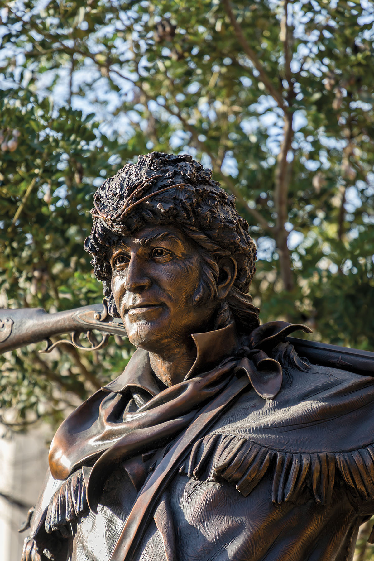 A bronze statue in front of bright green trees