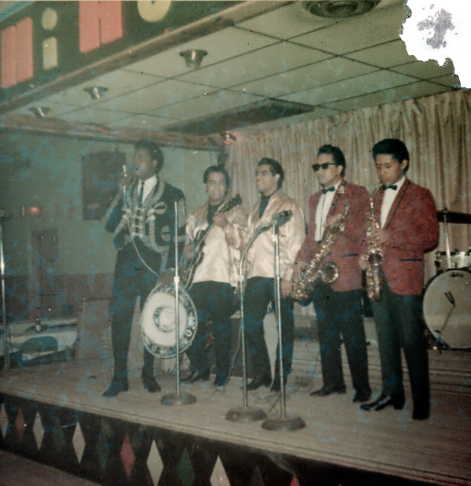 A group of men in colorful suit jacket perform in a dark setting