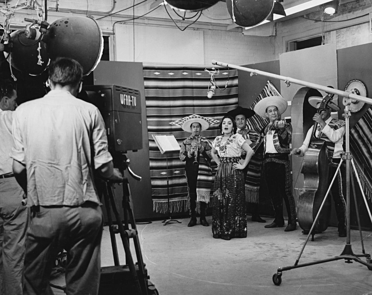 A woman sings into a microphone inside of a television studio