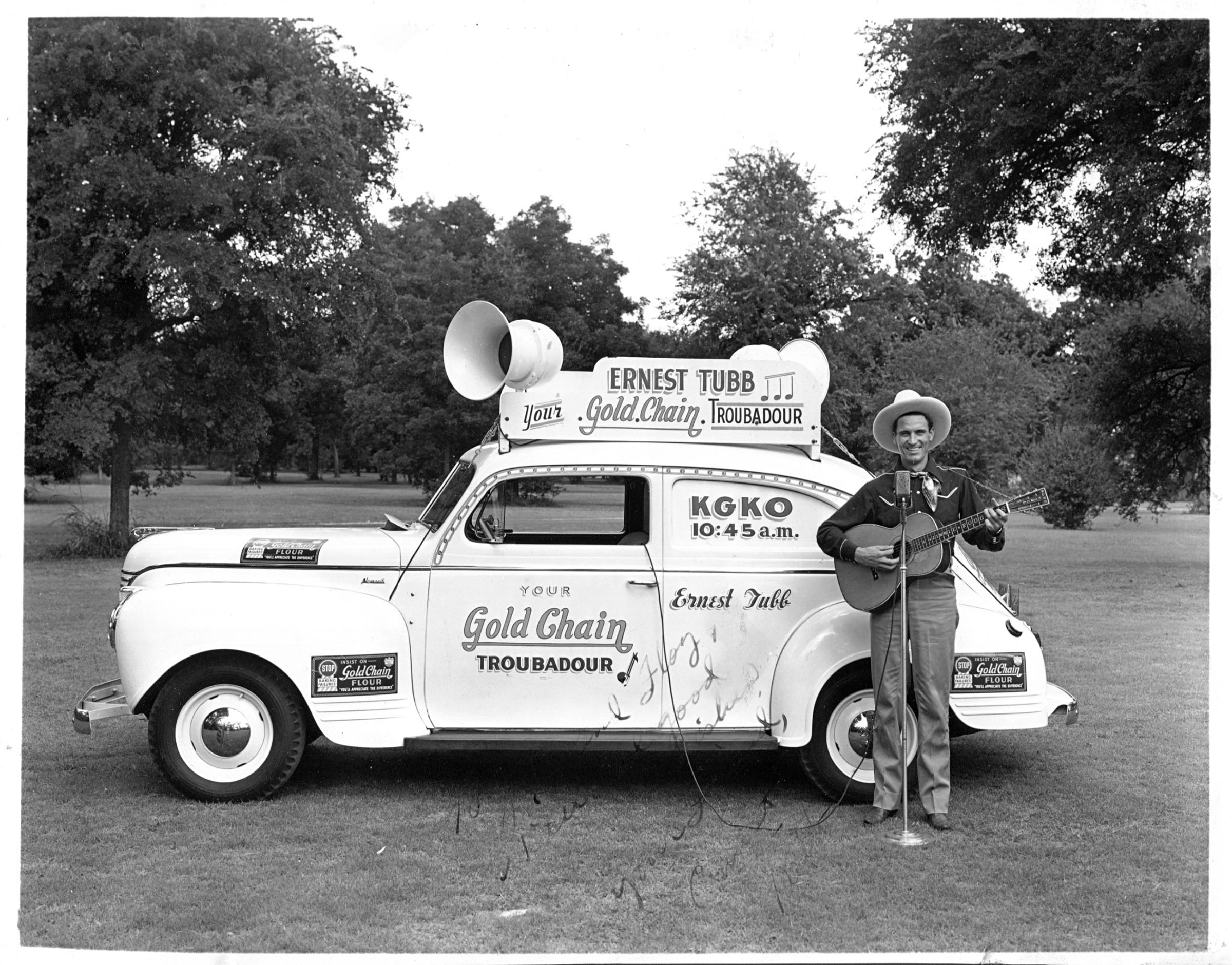 A man stands next to an old car decorated with music insignia