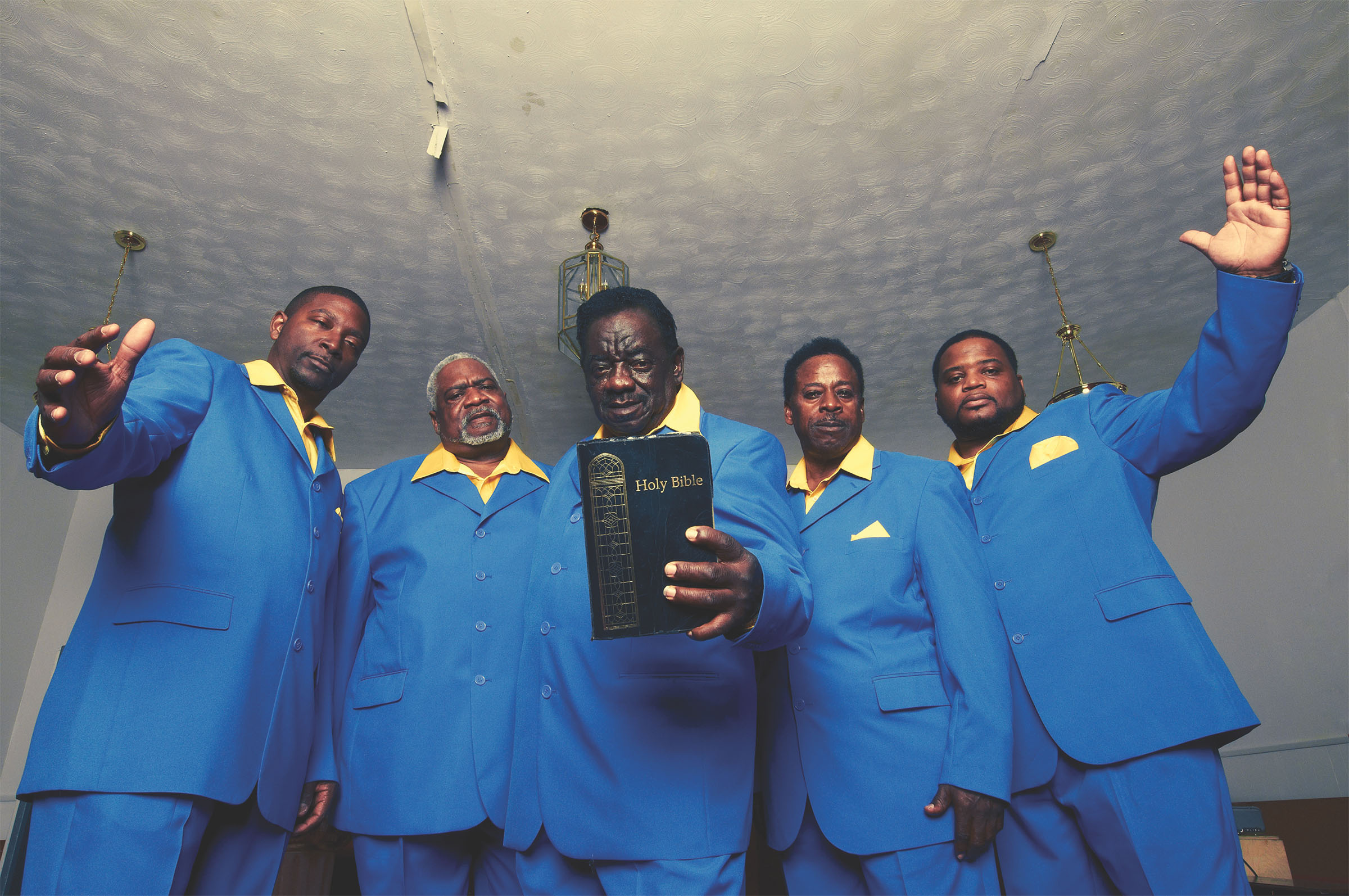 A group of men in blue gospel choir clothes hold a bible
