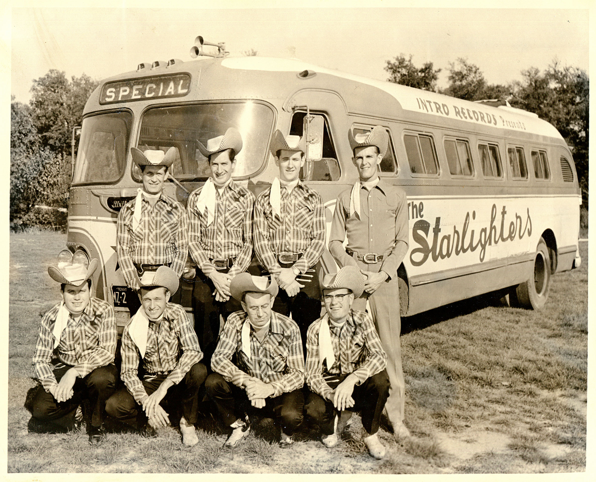A group of people in bent, curved cowboy hats stand out front of a bus
