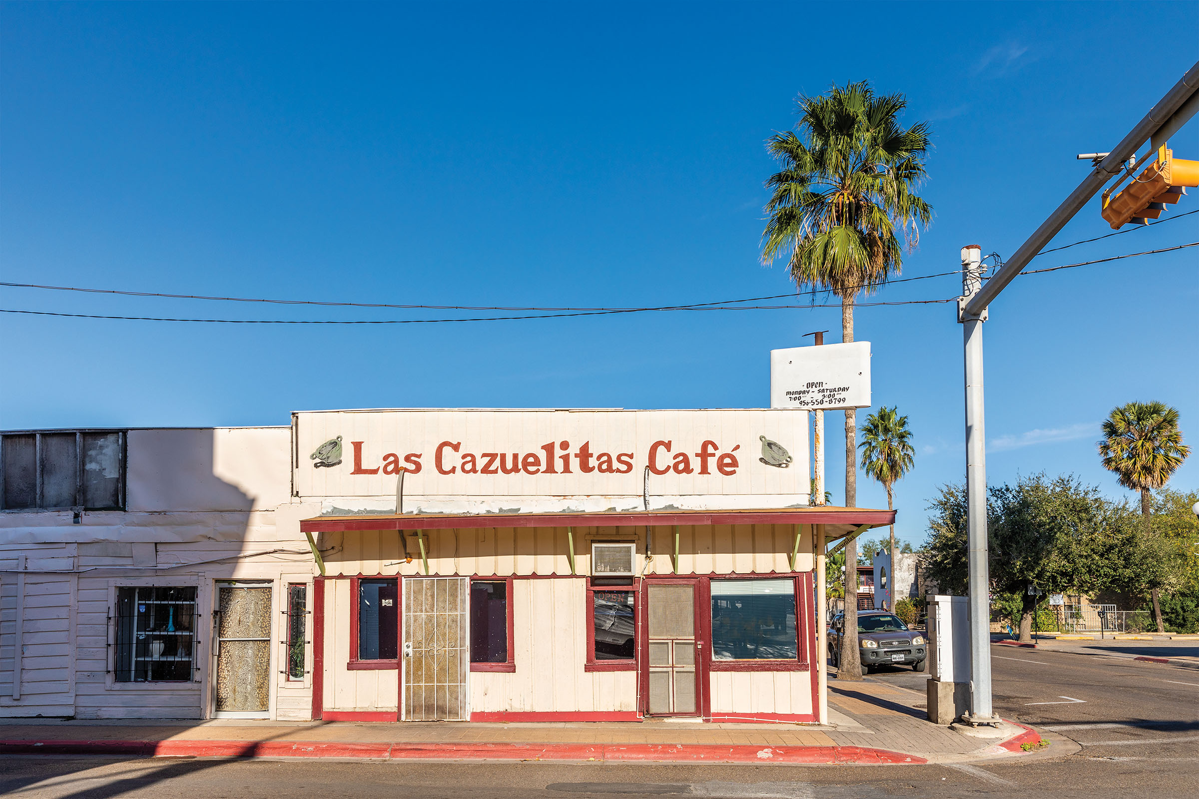 The exterior of a small pink and red building next to a tall palm tree