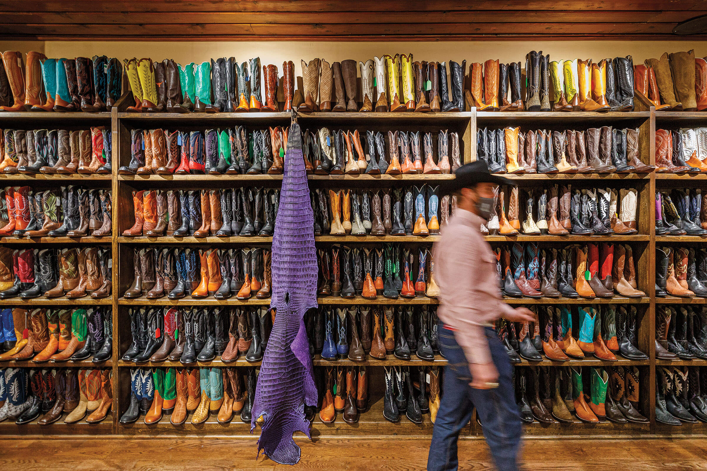 A man in a cowboy hat walks in front of a large wall of boots