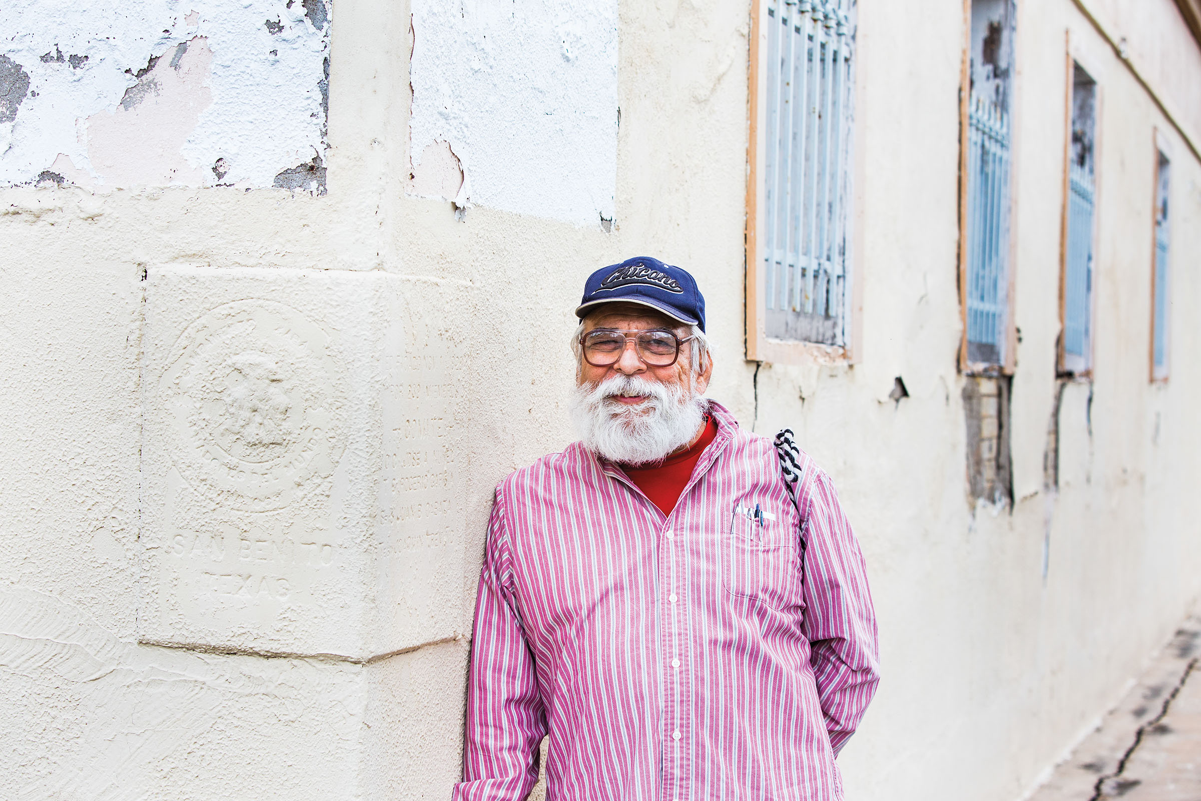 A man in a bright pink shirt and ball cap stands against a white wall