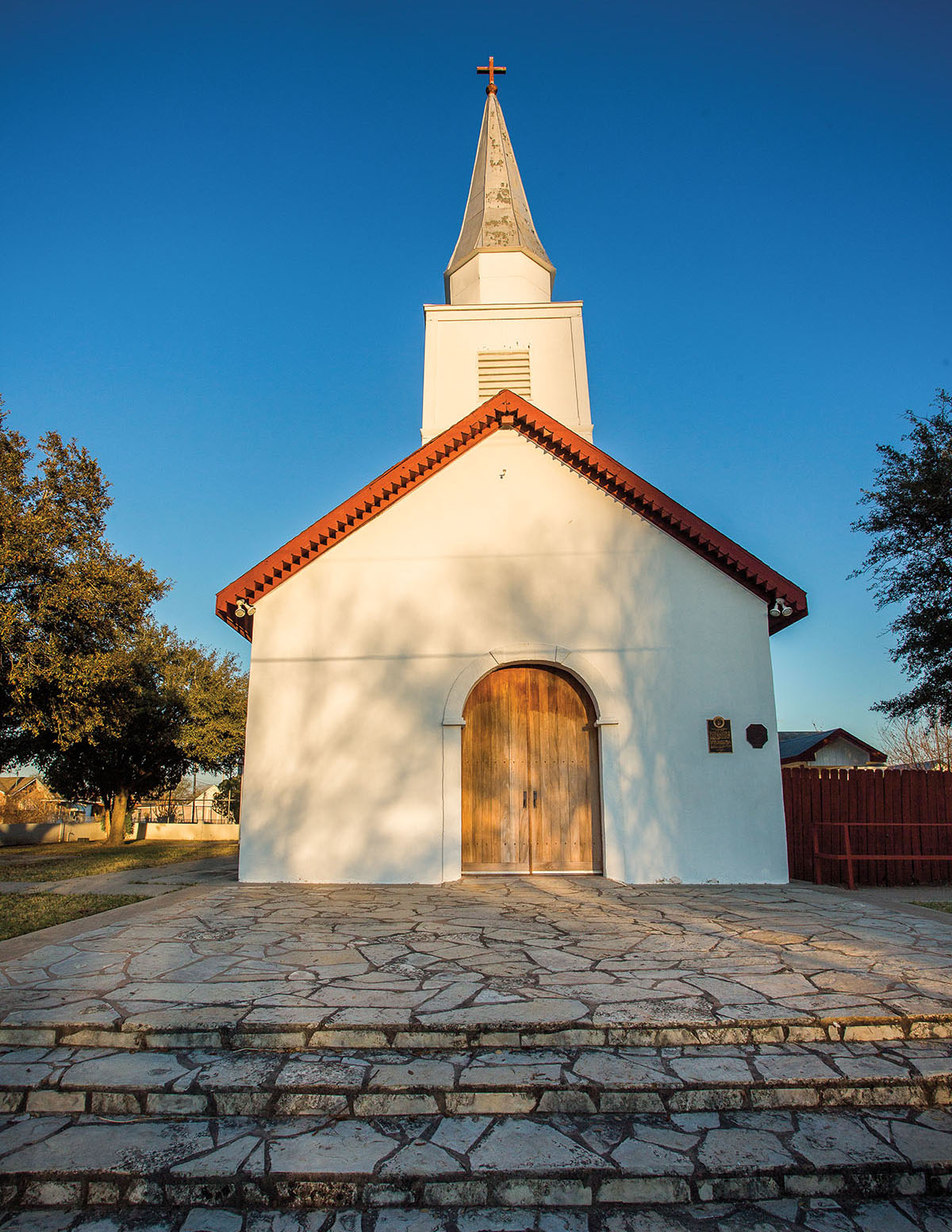 A white chapel with a brown wooden door on top of flat stones