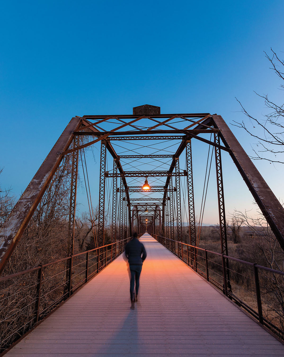 A sihlouetted figure walks across a suspension bridge in blue and pink light 