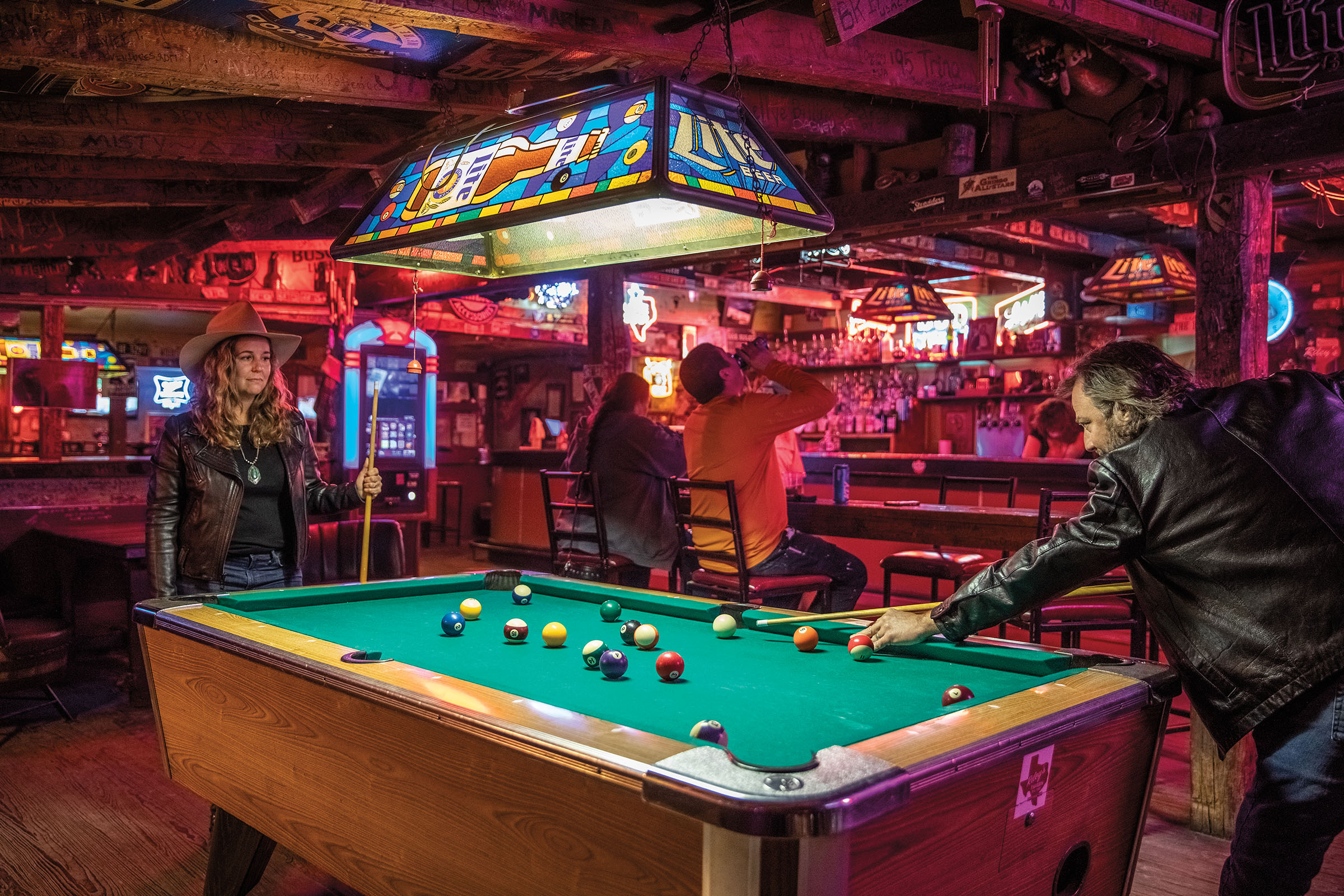 People play pool in a purple-lit bar