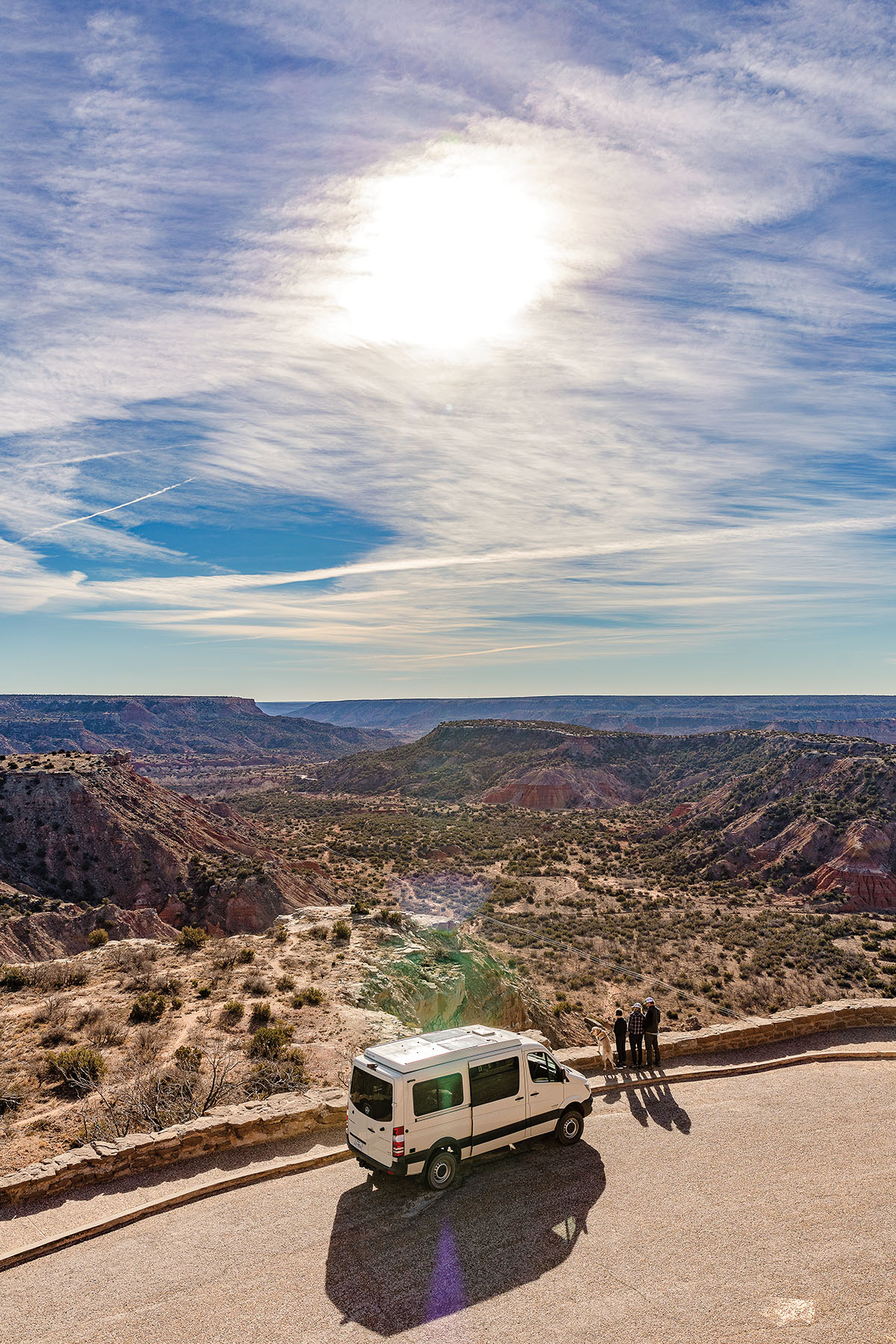 A white camper van parked by the side of the road overlooking a vast canyon under blue sky