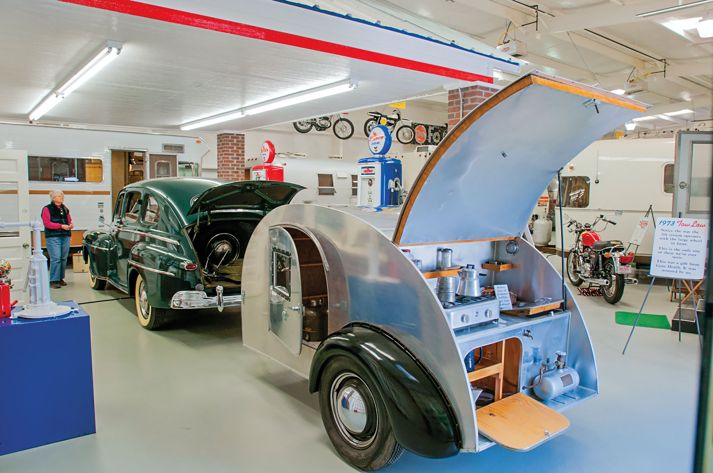 A silver trailer behind a green old fashioned car parked in a museum