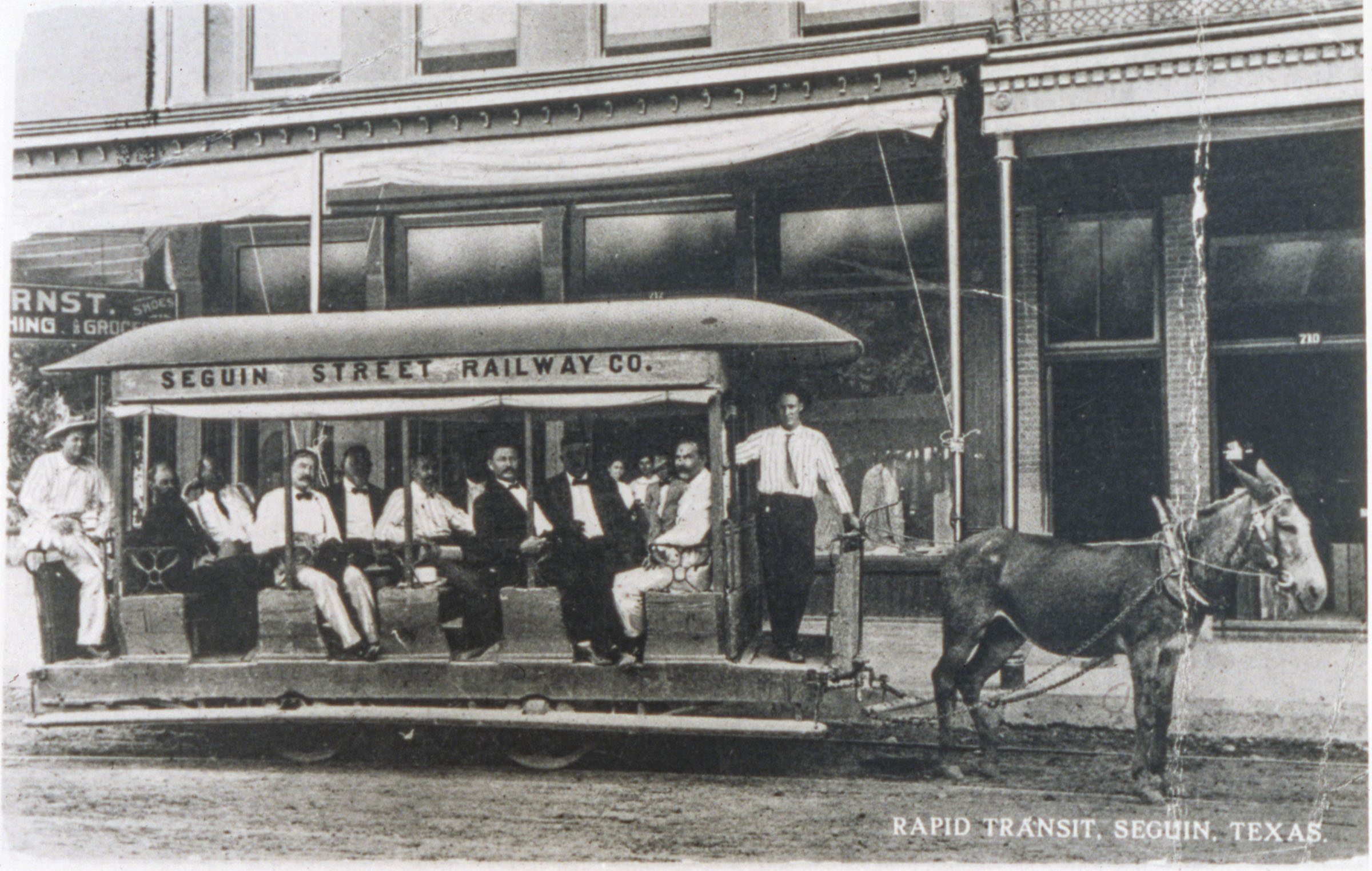 People dressed in shirts and ties sit on a streetcar in a historic photograph
